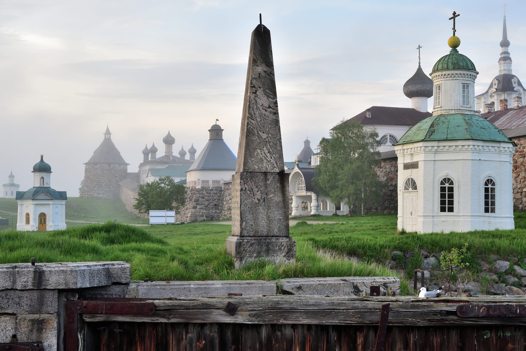 White onion-domed monastery buildings and a stone obelisk in mist