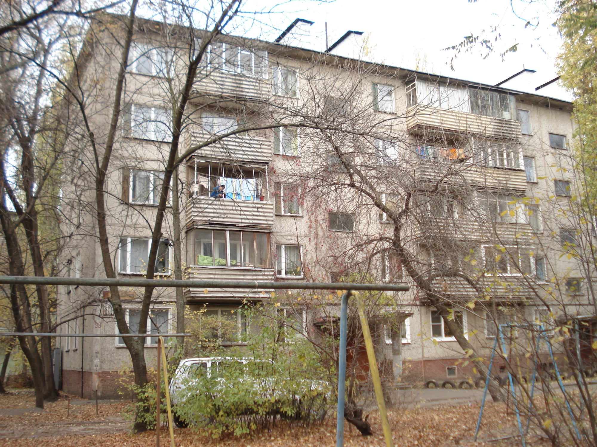 A weathered five-storey Soviet-era apartment block with balconies, seen through bare trees, with a children's playground in front