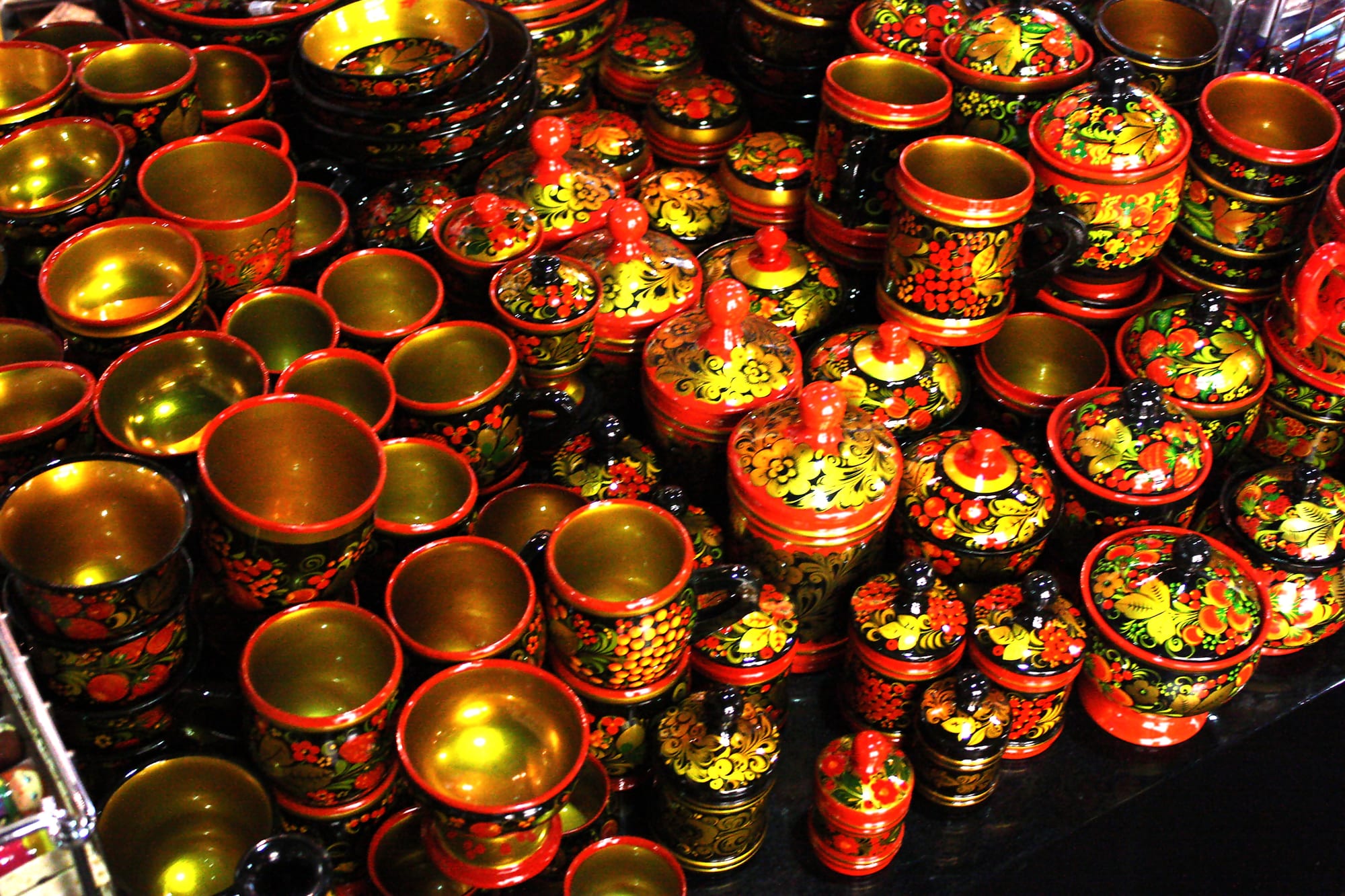 Dozens of wooden cups, bowls and lidded pots painted in red, black and gold with berry and leaf patterns crowded together on a shop shelf