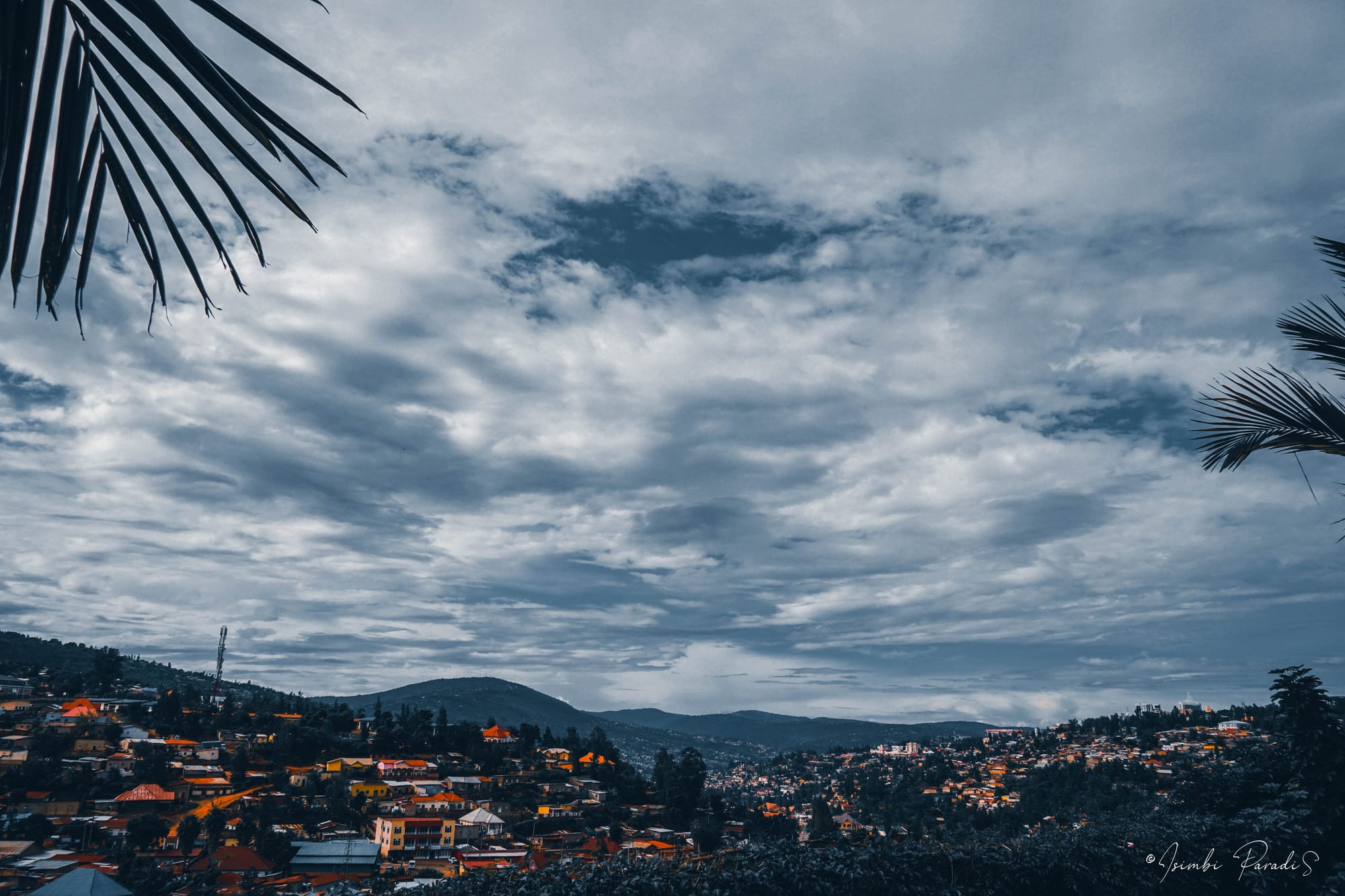 The city of Kigali spread across a series of steep green ridges and valleys under a cloudy sky