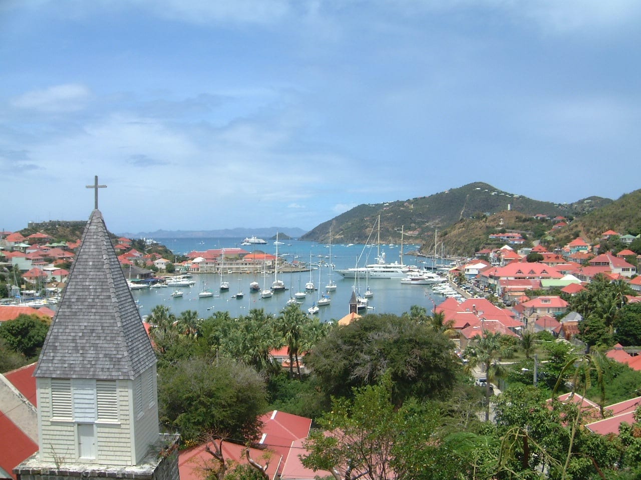 A row of yachts moored in a small harbour surrounded by hillside buildings