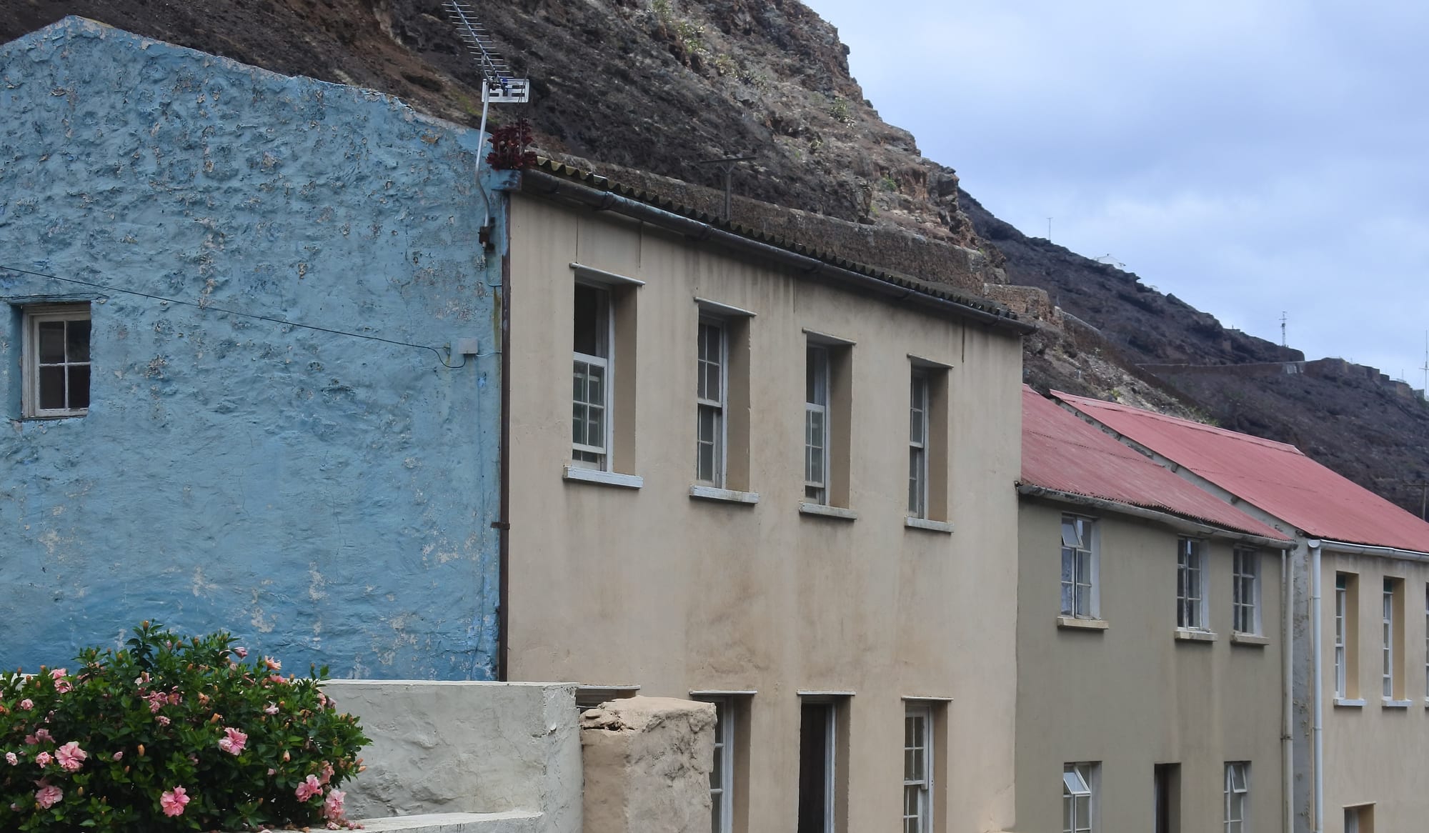 A row of pastel-coloured plastered houses built directly against a steep bare cliff face
