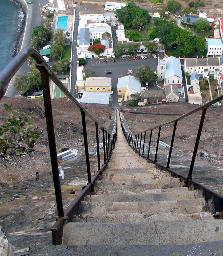 A very long, steep staircase running straight up a cliff face beside a town