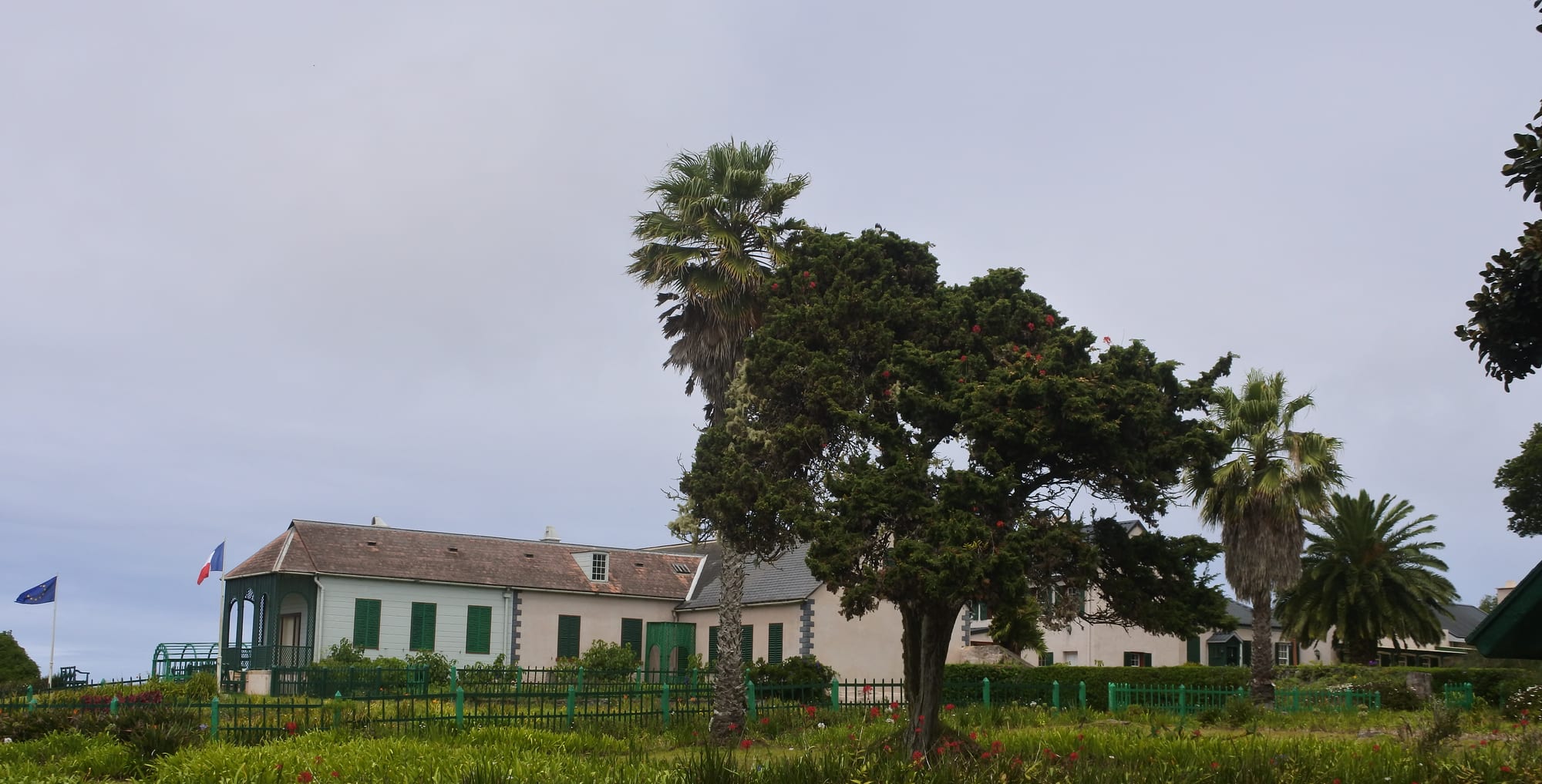A long, low white colonial house with a veranda surrounded by lawns and trees on a windswept plateau