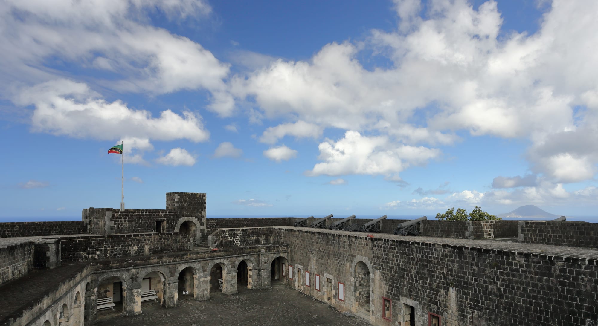 A massive stone fortress complex on a hilltop overlooking the Caribbean sea