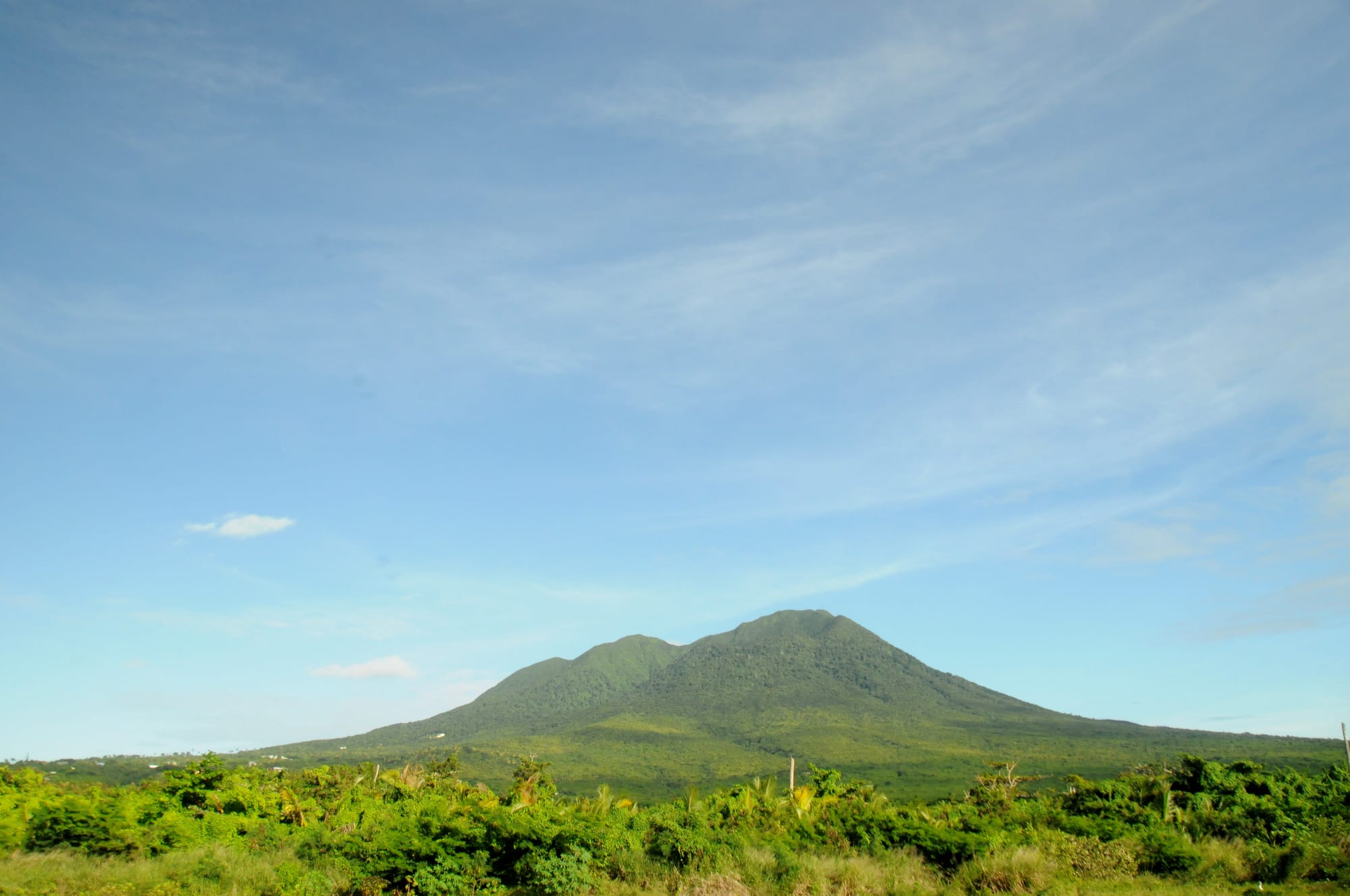 A cloud-wrapped volcanic peak rising above a green coastline
