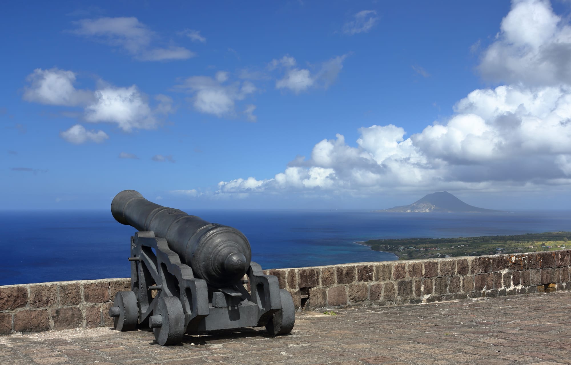A large stone fortress with bastions and cannon on a steep green hill overlooking the sea on Saint Kitts