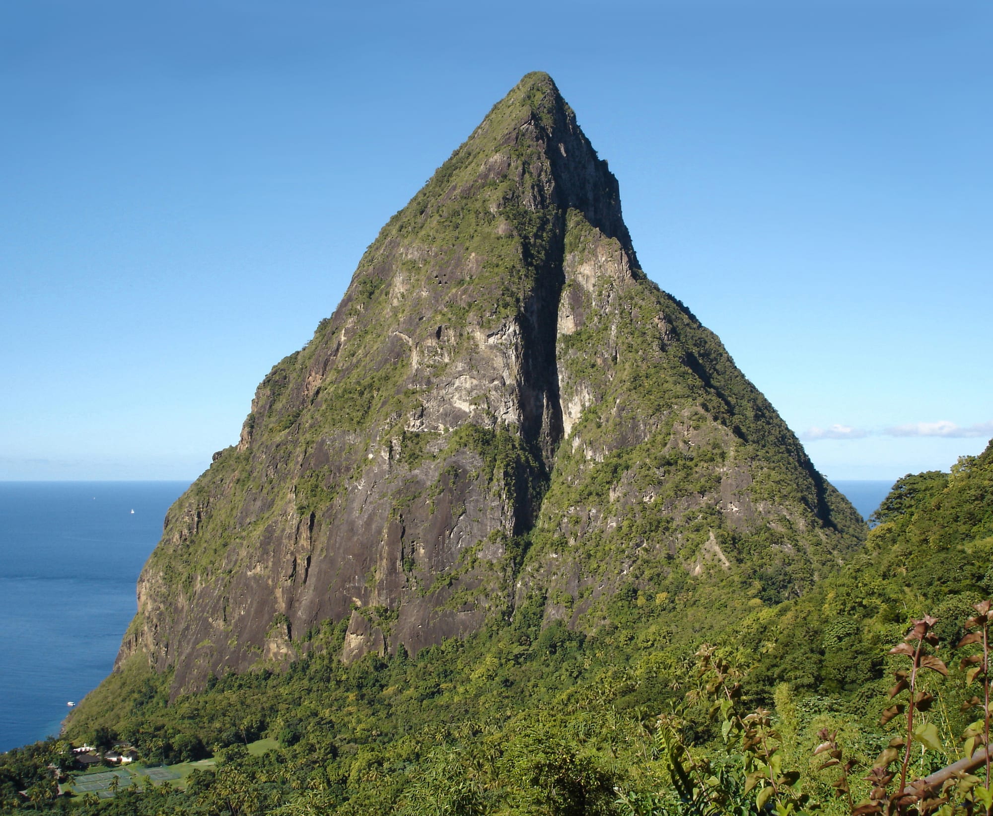 A single steep volcanic peak rising above a coastal town and palm trees