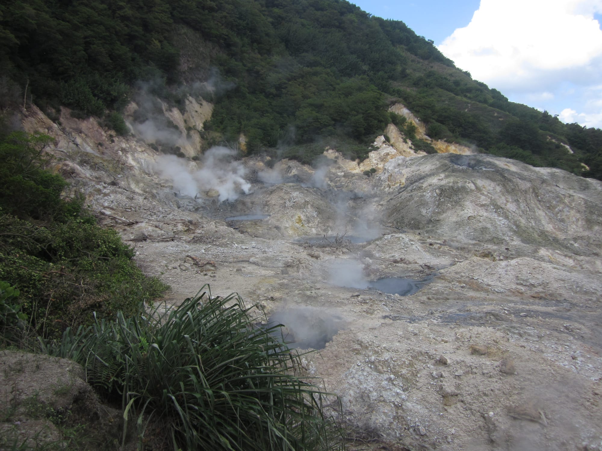 A steaming volcanic crater with mineral-stained rock and pools