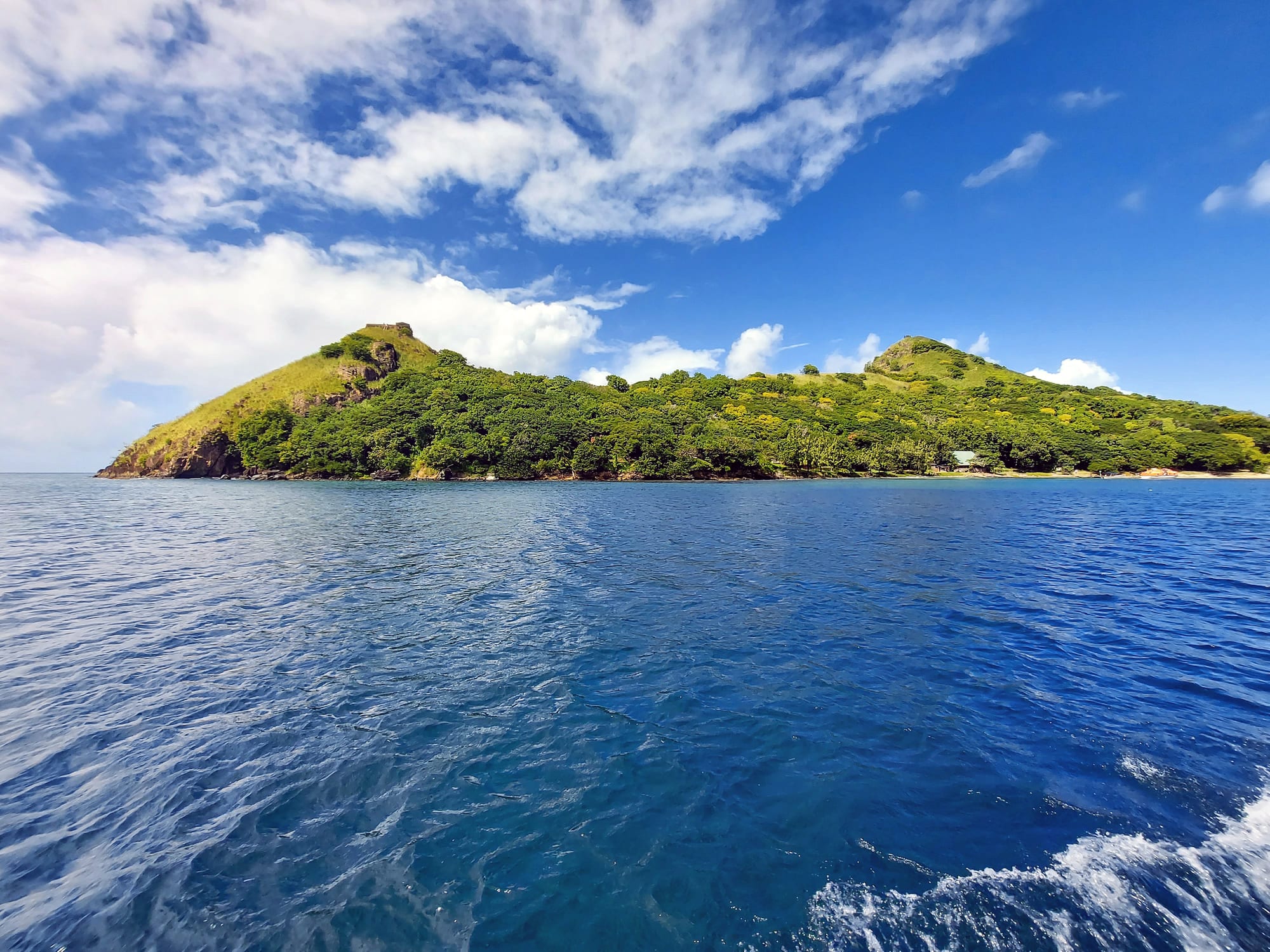 A grassy headland with the stone ruins of a fort, joined to the Saint Lucia mainland by a low causeway
