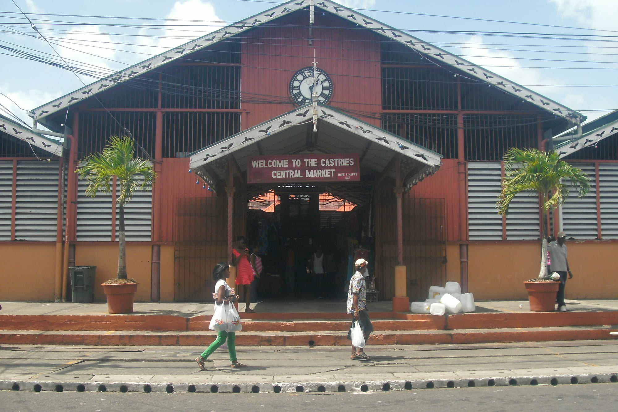 The red-roofed Castries Central Market building with its clock tower, shoppers carrying bags crossing the street in front