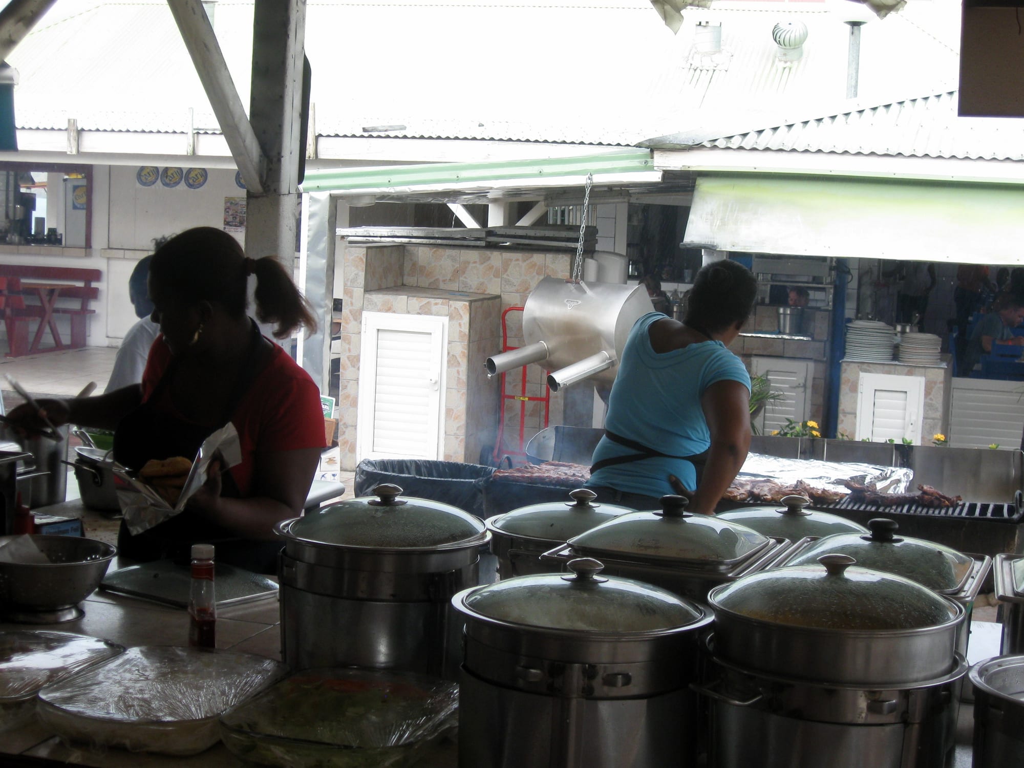 Cooks working over steaming pots and a smoking grill at an open-air lolo food stall in Grand Case