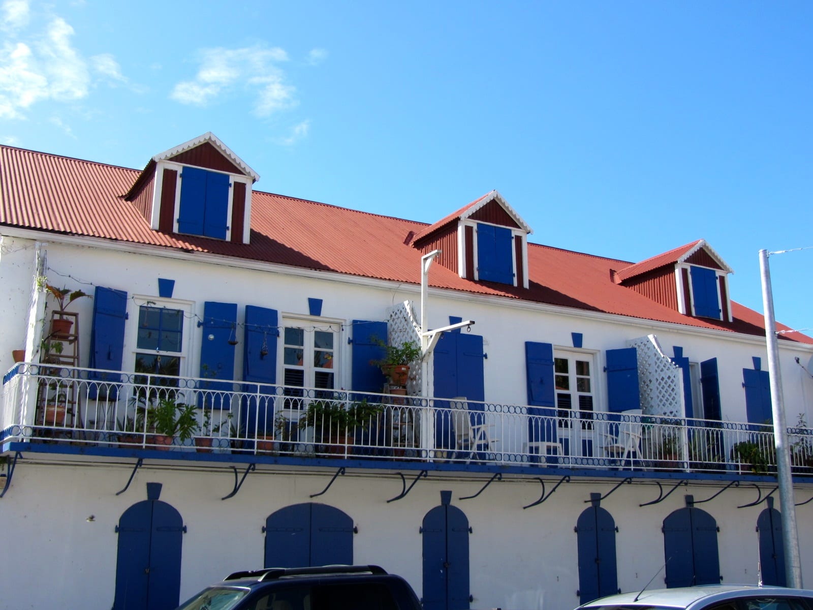 A white building with a red corrugated roof and rows of blue-shuttered dormer windows and balcony doors in Marigot