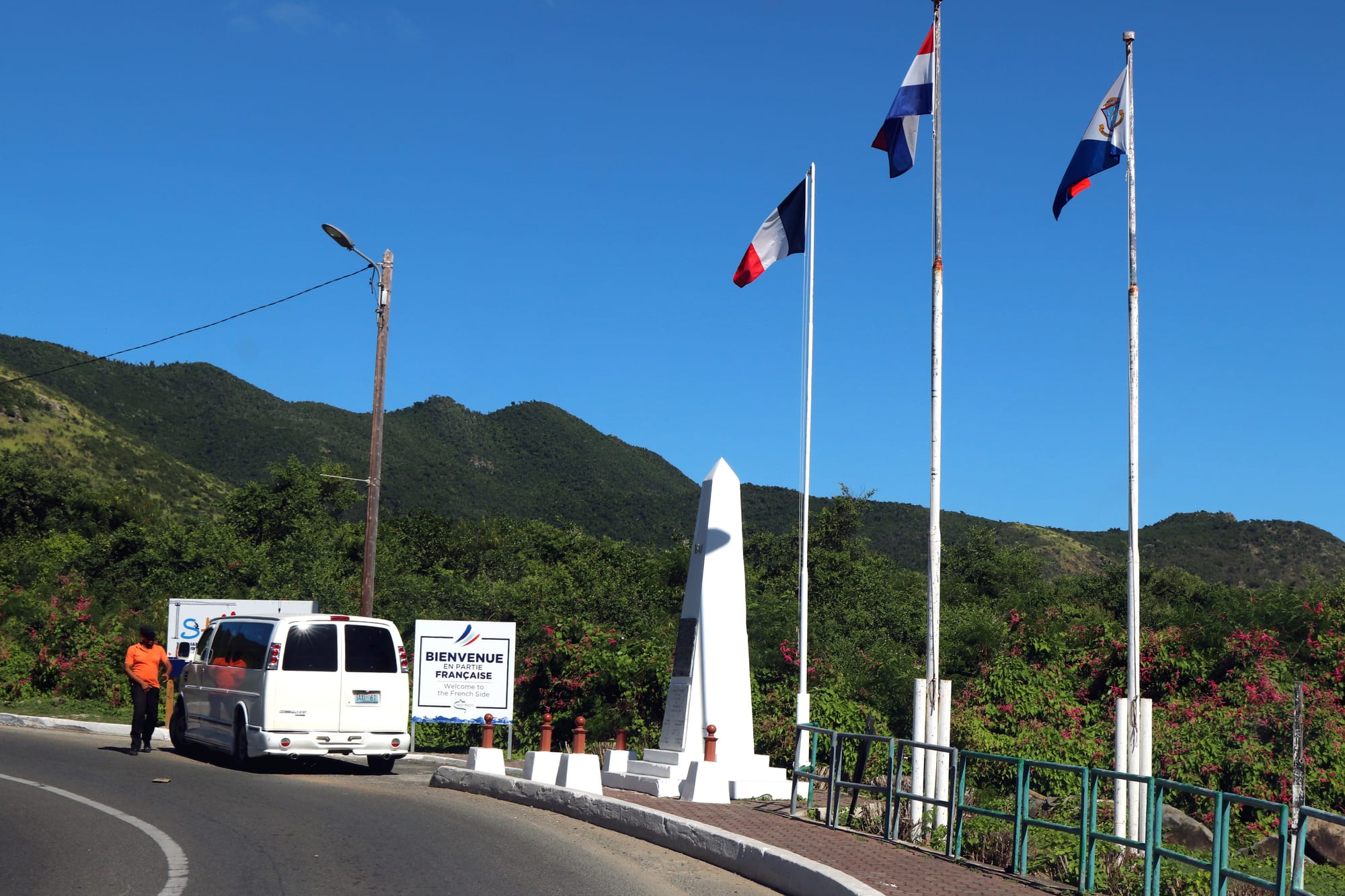 A roadside monument reading 'One Caribbean Island, Two Countries' marking the open border between French and Dutch Saint Martin