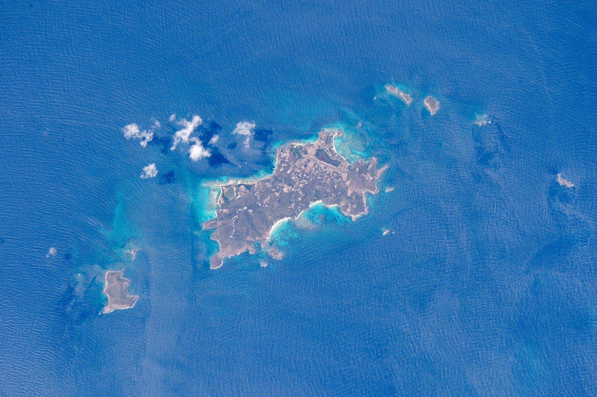 A satellite view of a small green island surrounded by reef and turquoise water