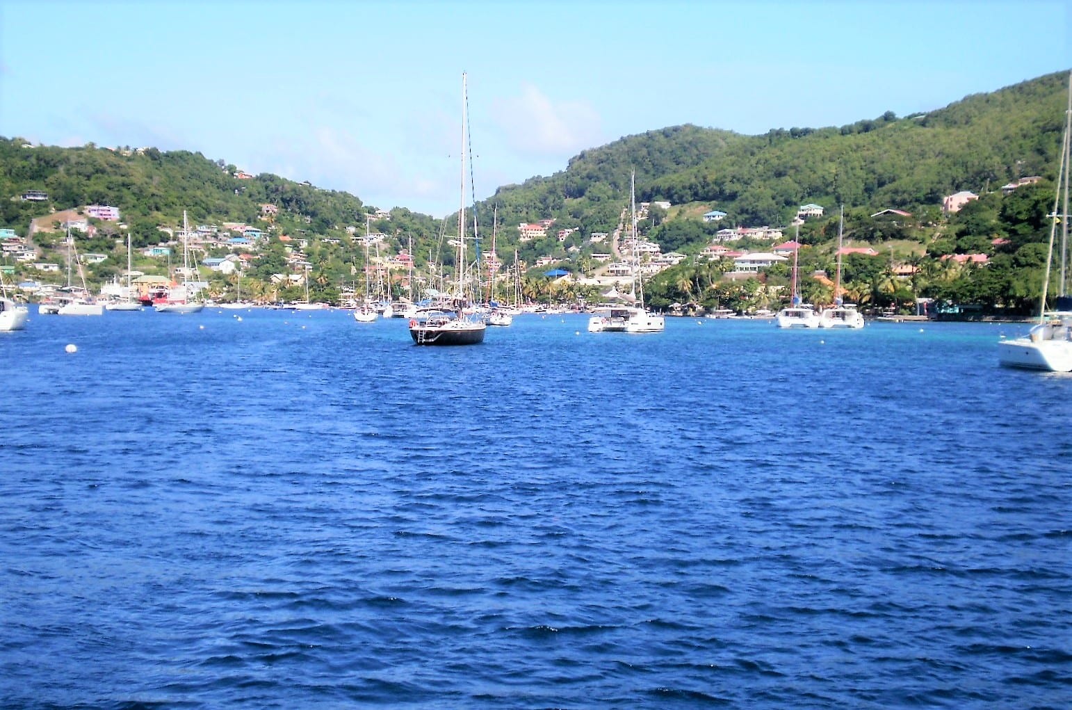 Sailing yachts anchored in the turquoise water of Admiralty Bay off Bequia, with a small town spread along the green hillside