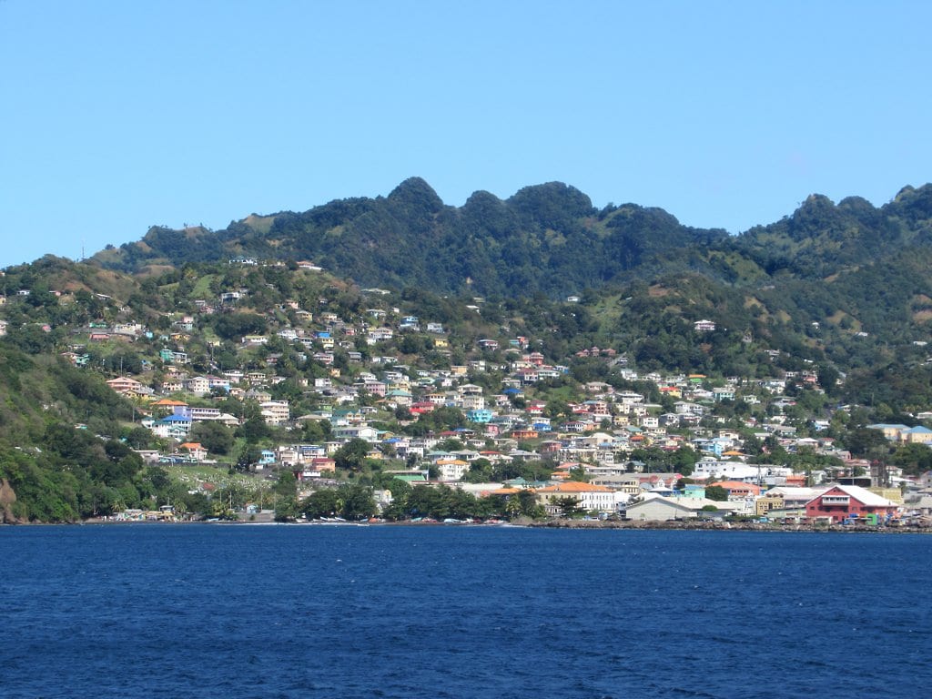 Kingstown seen from the water, a hillside covered in colourful houses beneath forested peaks under a clear blue sky