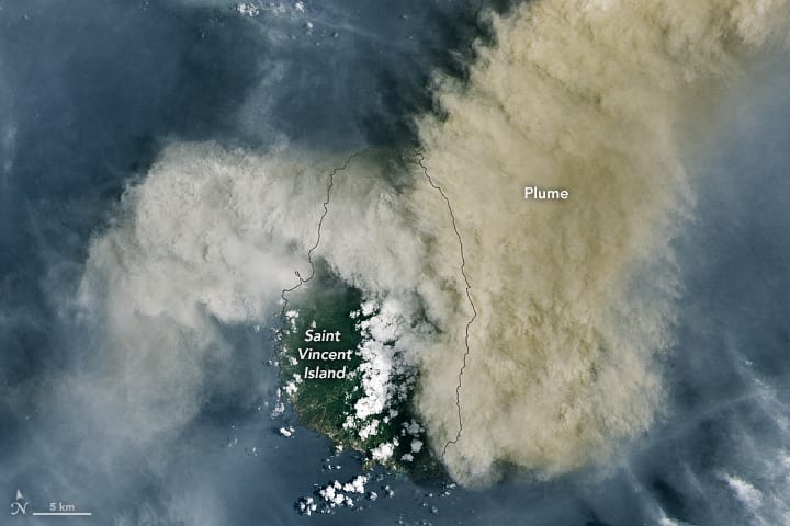 A satellite image of Saint Vincent almost entirely covered by a wide brown ash plume streaming east over the sea