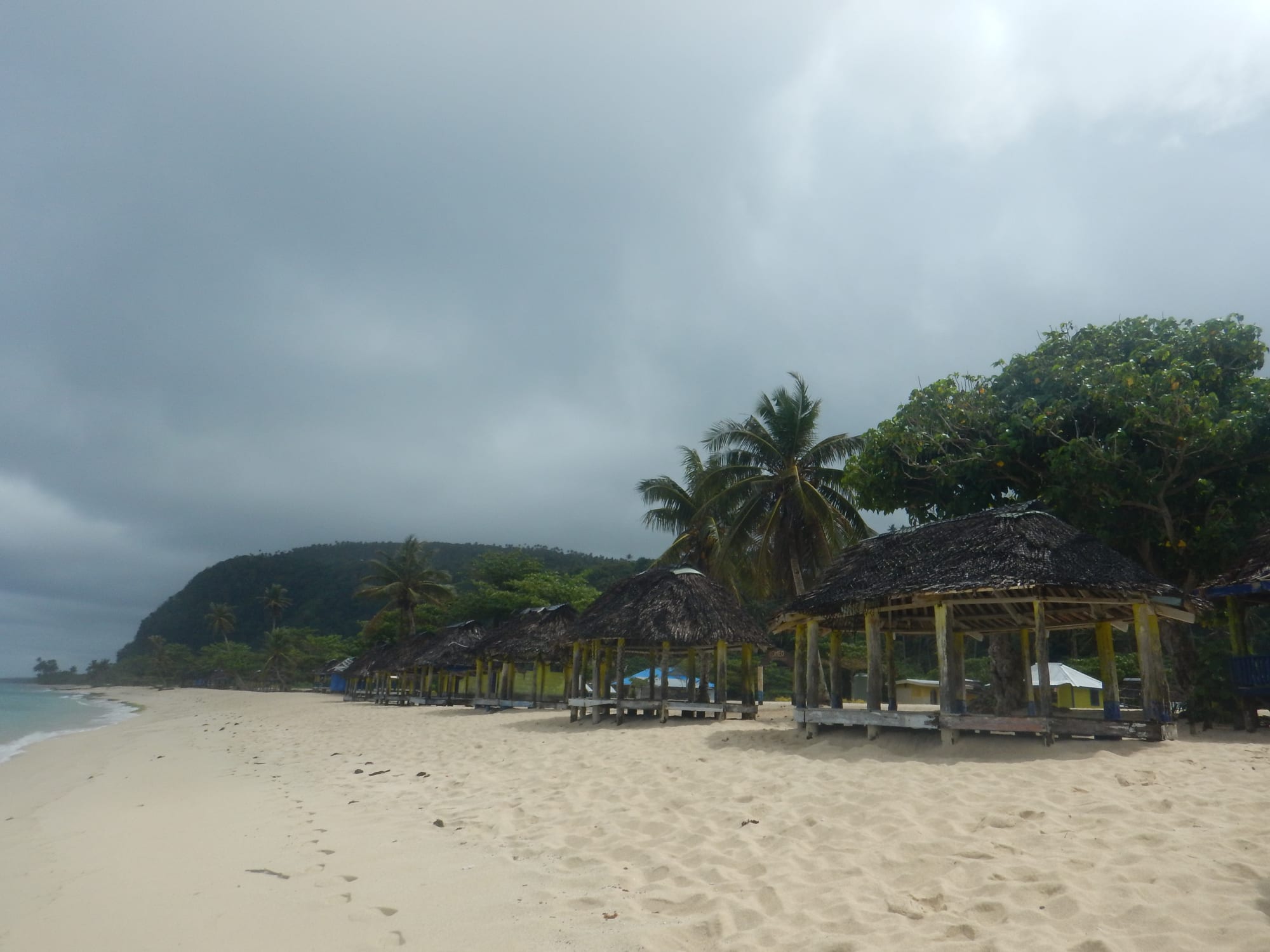 Traditional open-sided beach huts along a white sand tropical beach