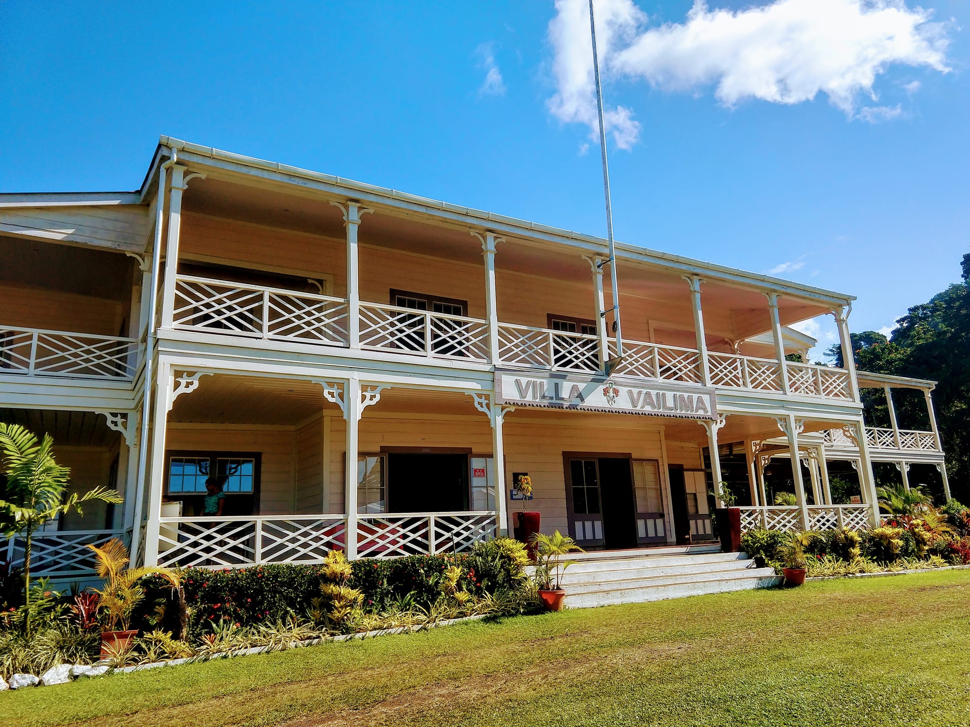 A grand colonial-era wooden house surrounded by tropical gardens