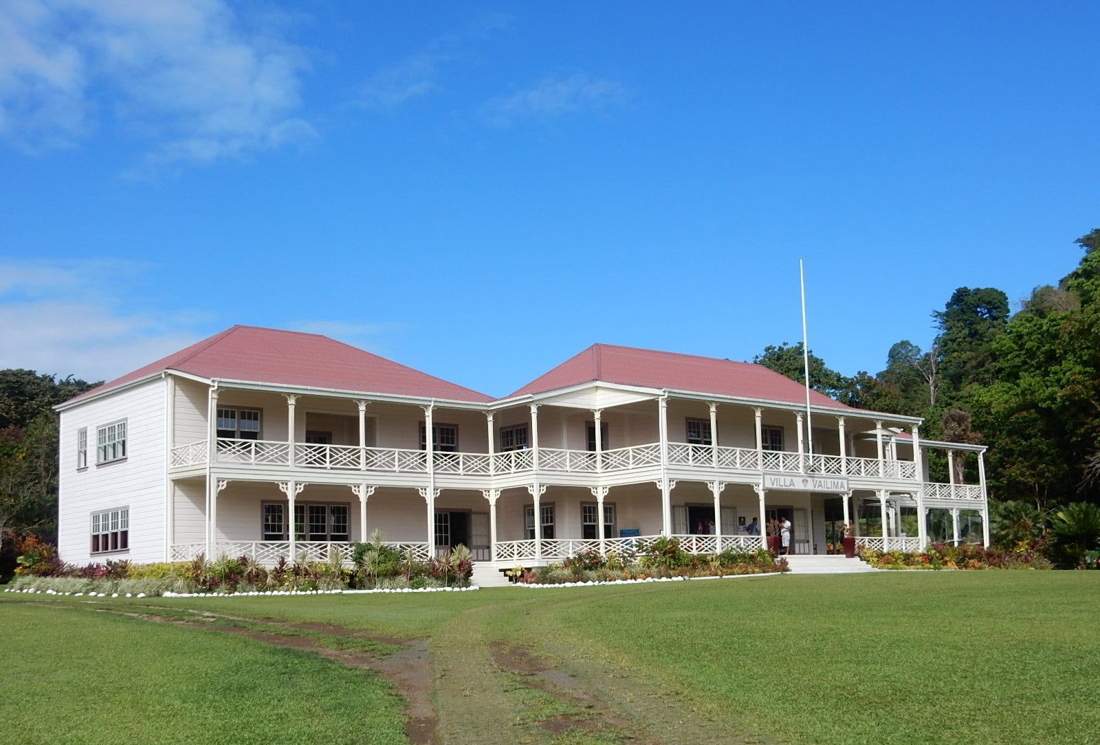A large colonial villa with wide verandahs set among lawns and tropical trees below a forested ridge