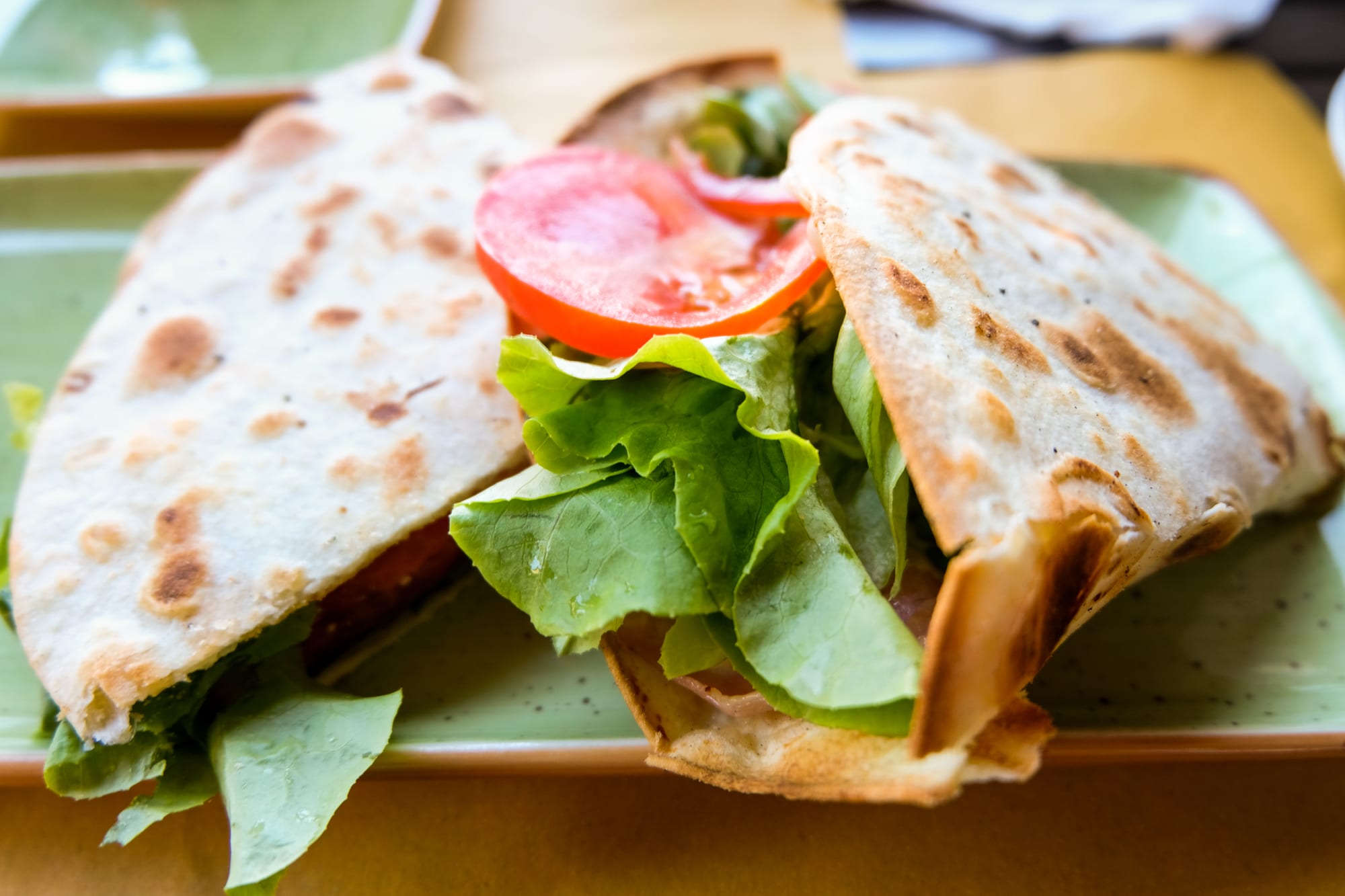 A folded, griddle-marked flatbread filled with lettuce and tomato slices on a green plate