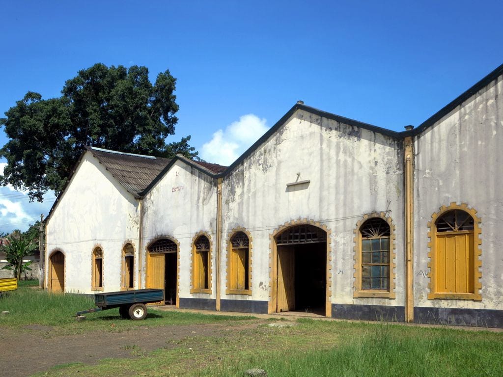 A long, decaying colonial-era warehouse building with arched openings on a former cocoa estate