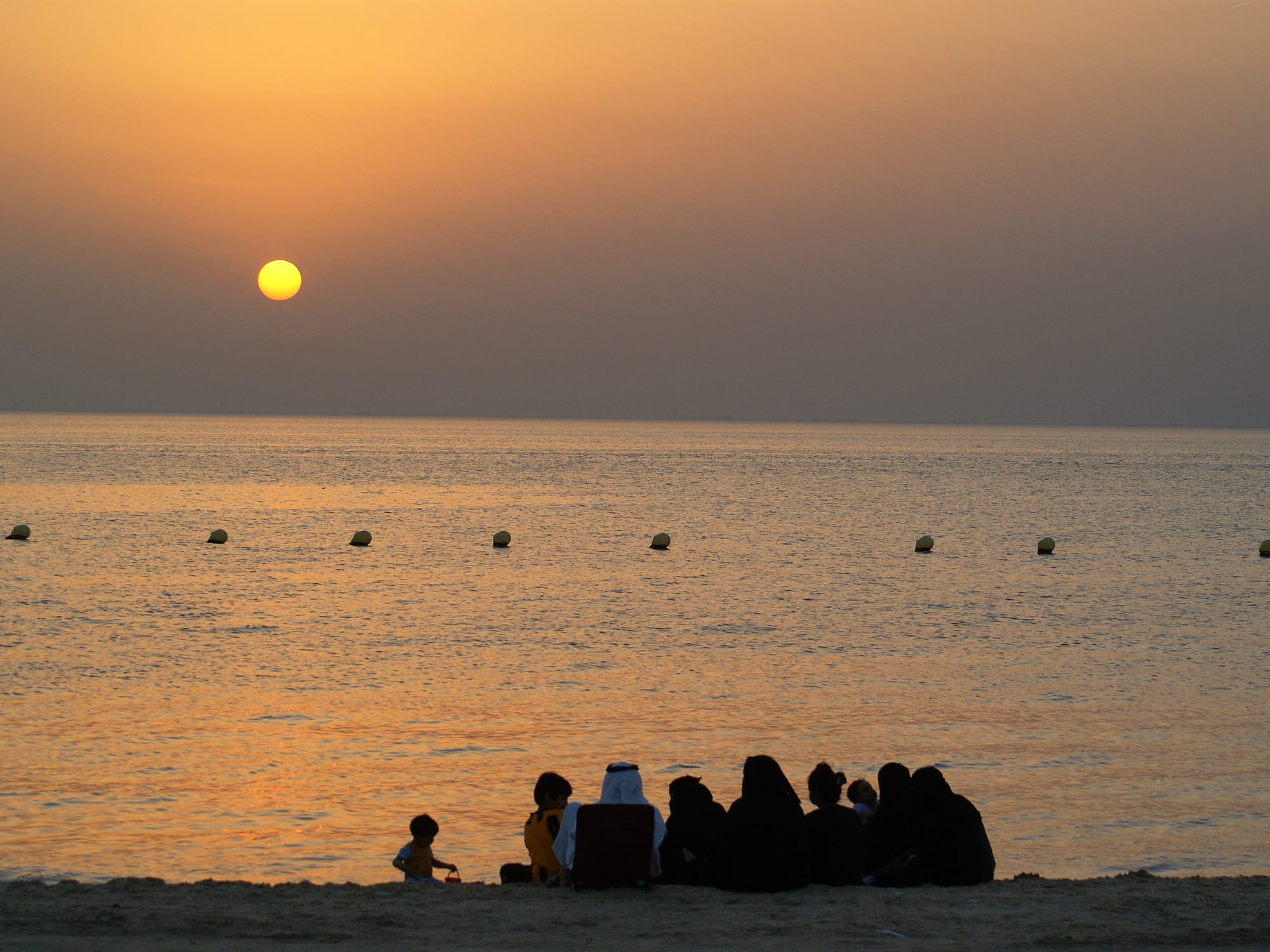 A family sits together in silhouette on a beach watching the sun set over the sea
