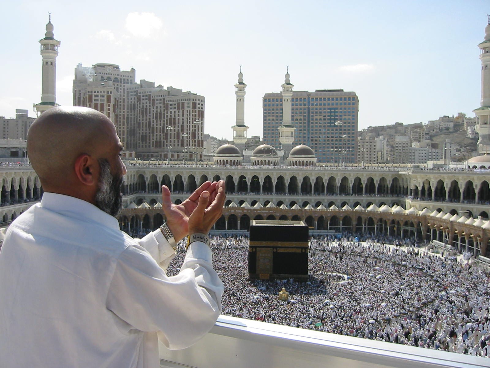 A vast mosque courtyard filled with worshippers around a central black cube structure