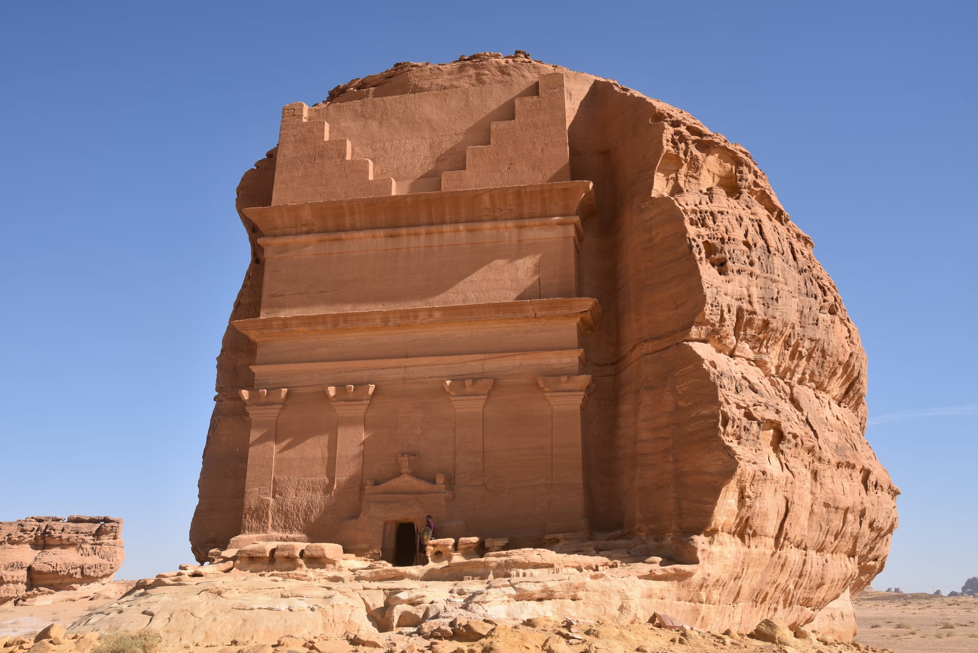 A large, ornately carved tomb facade cut into a sandstone boulder in a desert landscape