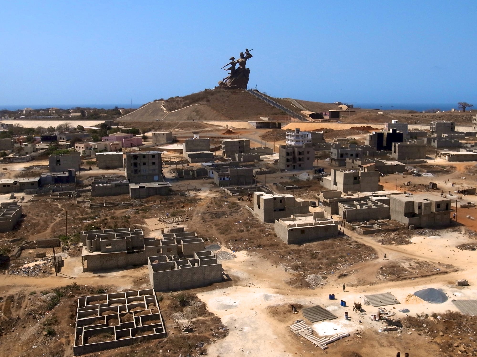 A massive bronze statue of a family group atop a hill, taller than surrounding buildings