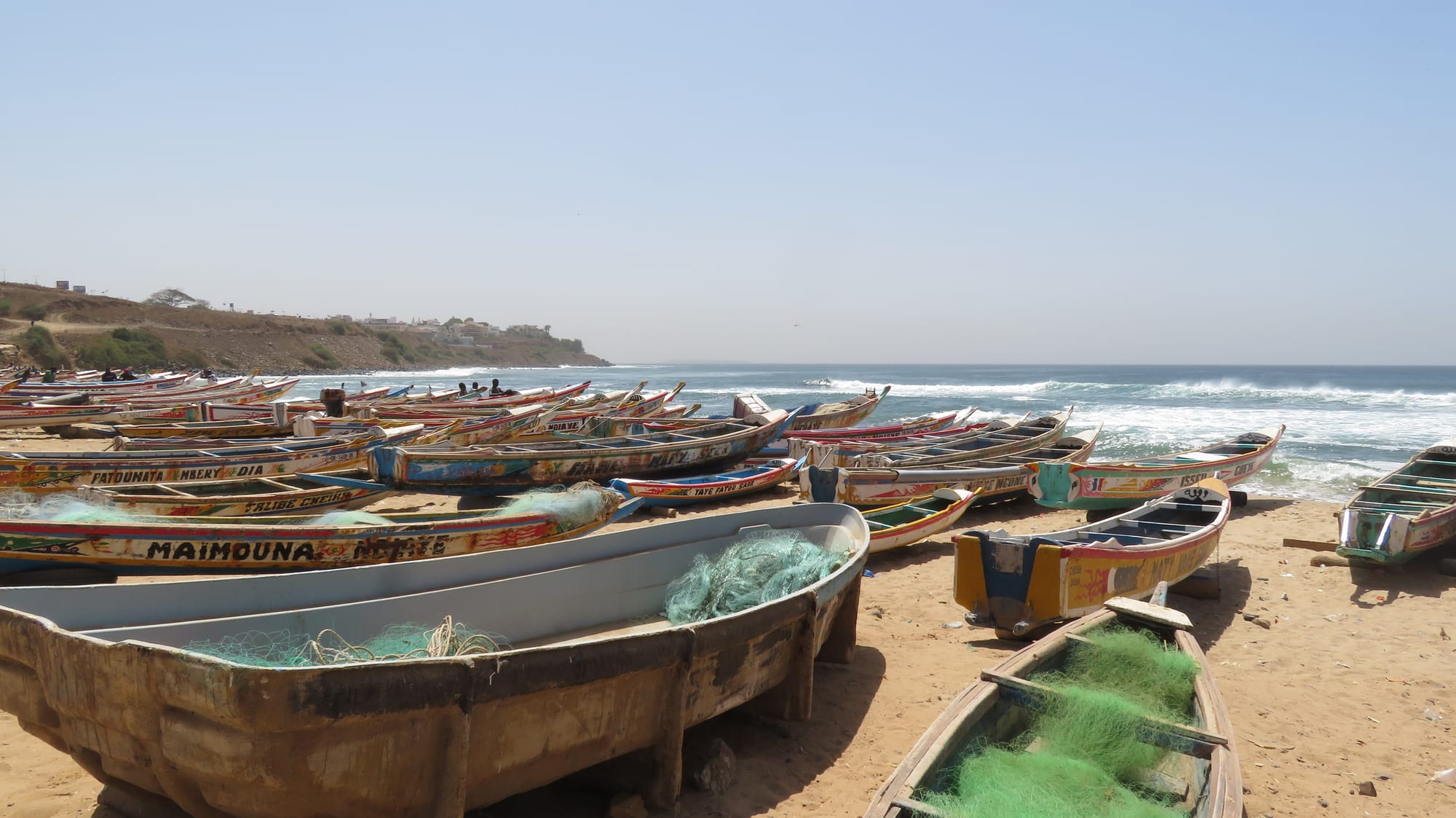 Dozens of brightly painted wooden fishing pirogues lined up on a sandy beach beside the sea