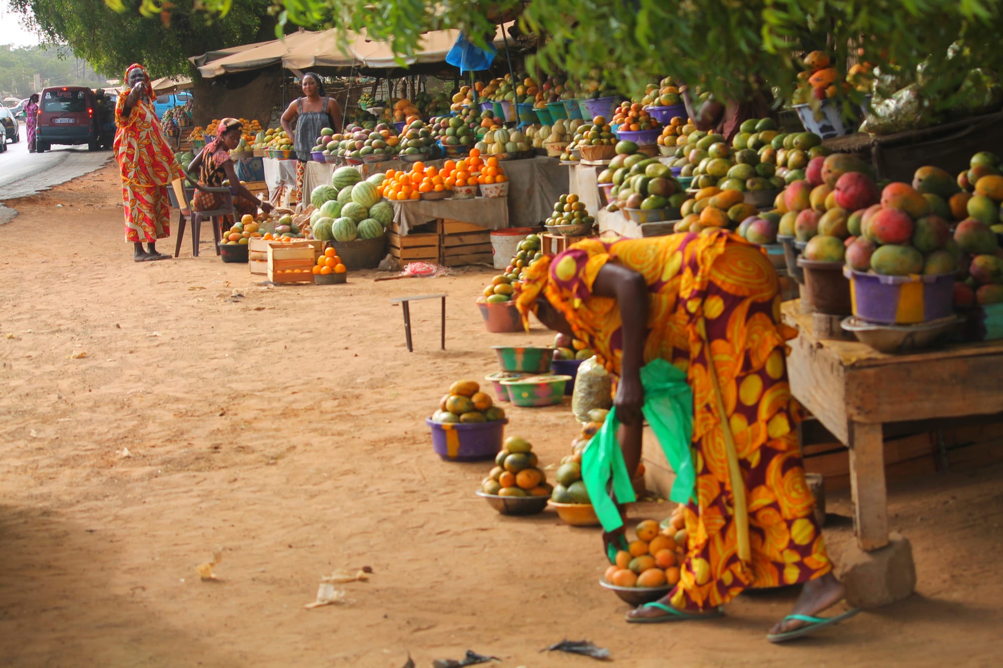 Women selling mangoes, watermelons and other fruit from stalls and baskets along a roadside market