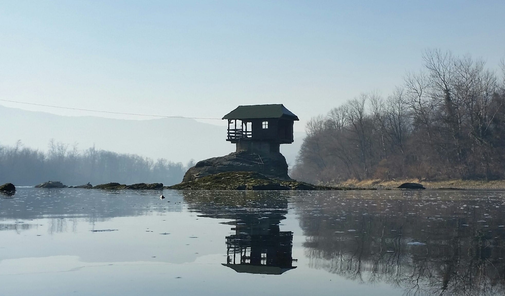 A small wooden house perched on a lone rock in the middle of a river