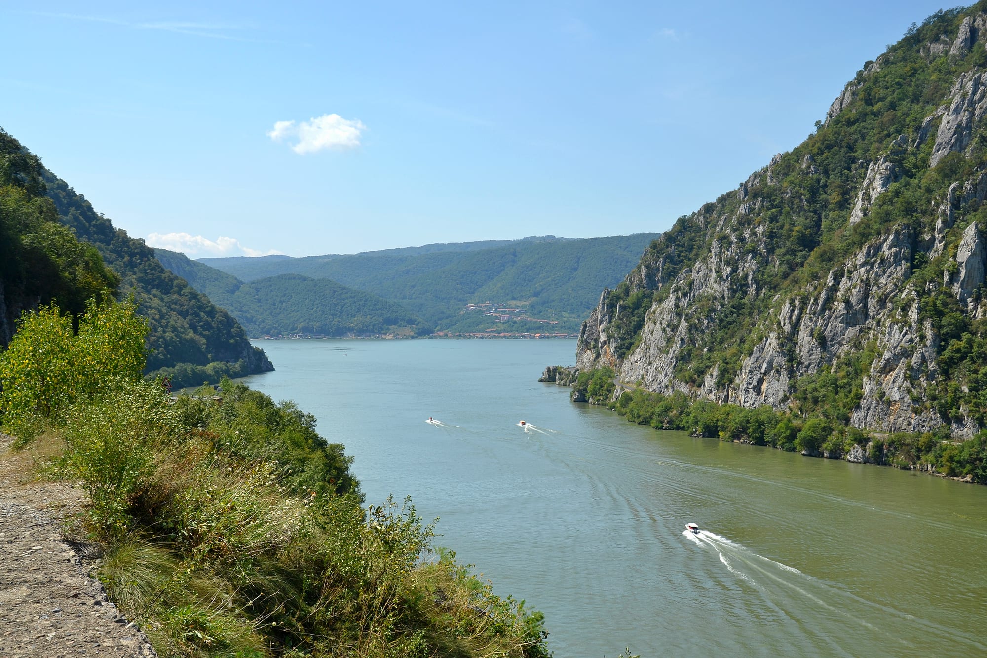 Speedboats crossing a wide river gorge between steep forested cliffs