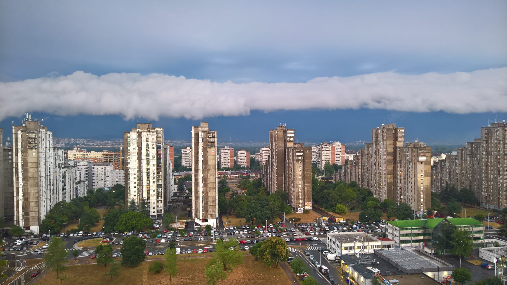 Rows of tall grey and beige apartment towers with a stormy sky above, cars parked along the streets between them
