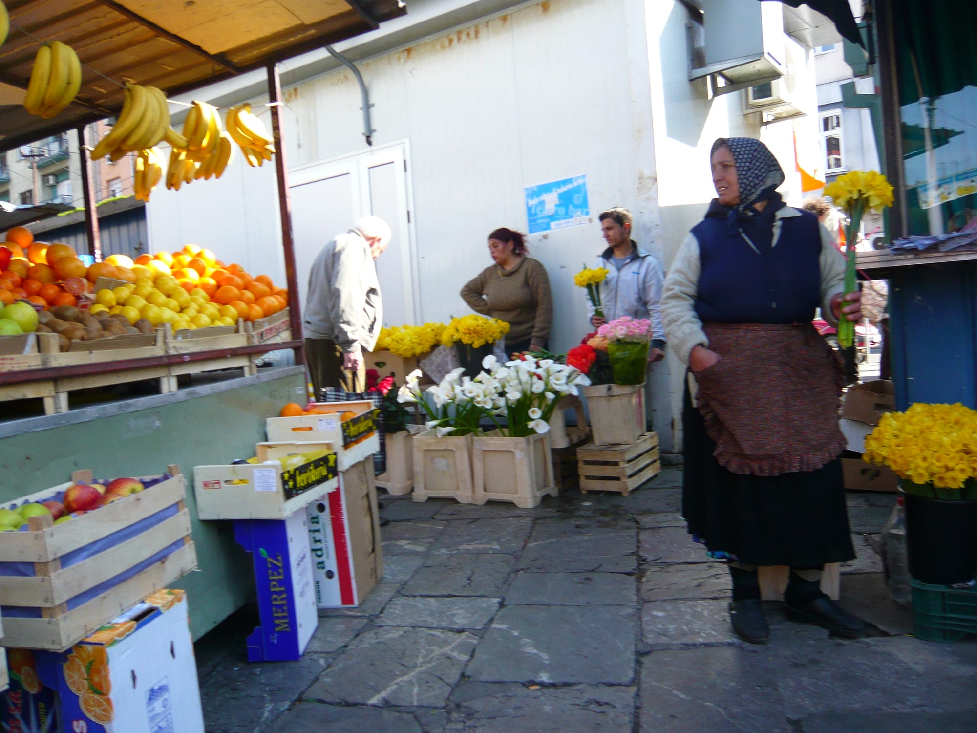 Vendors and shoppers among stalls of oranges, apples and cut flowers at Belgrade's Kalenić market