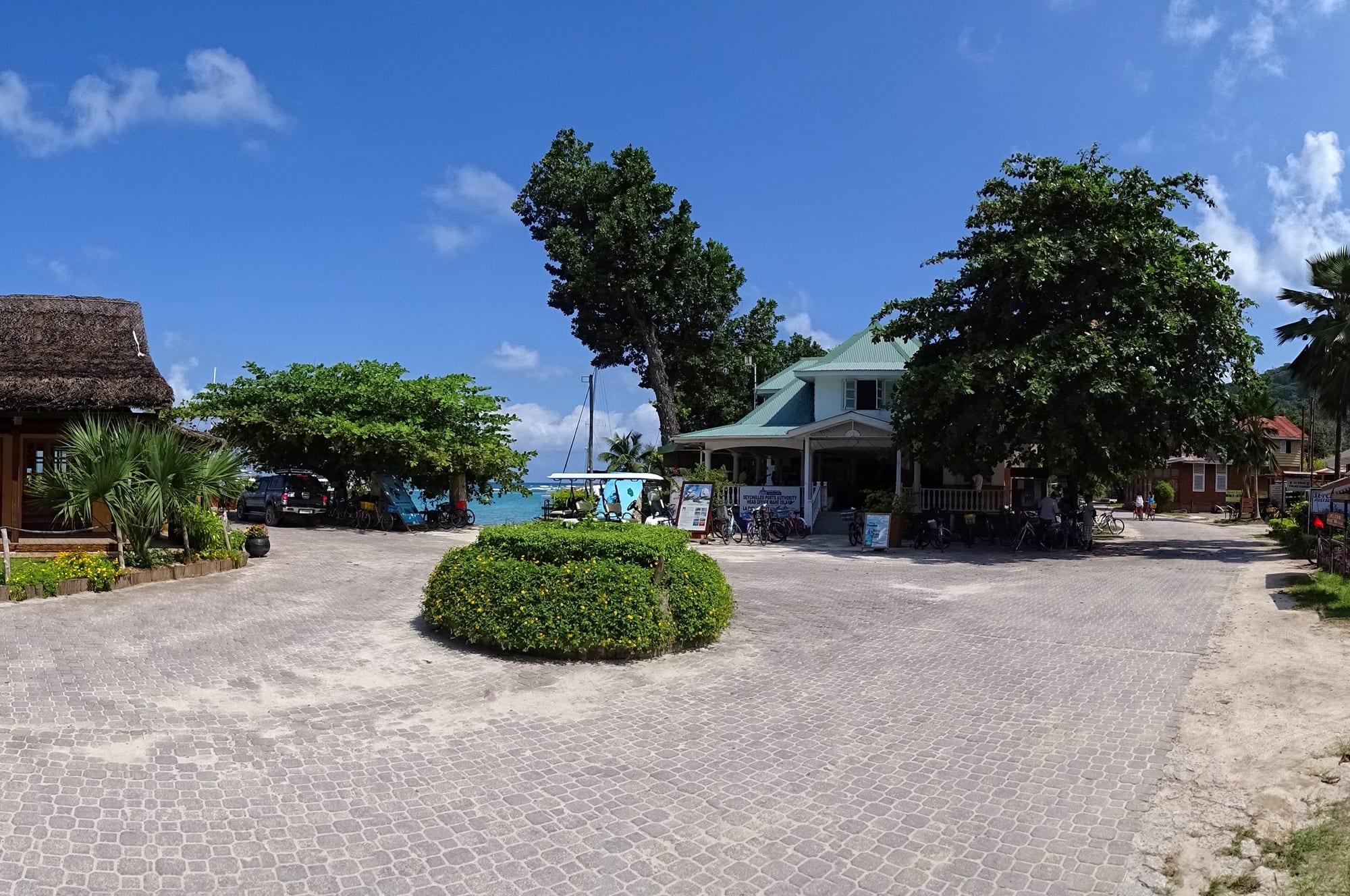 A paved square with parked bicycles outside buildings near a beach and turquoise sea on La Digue