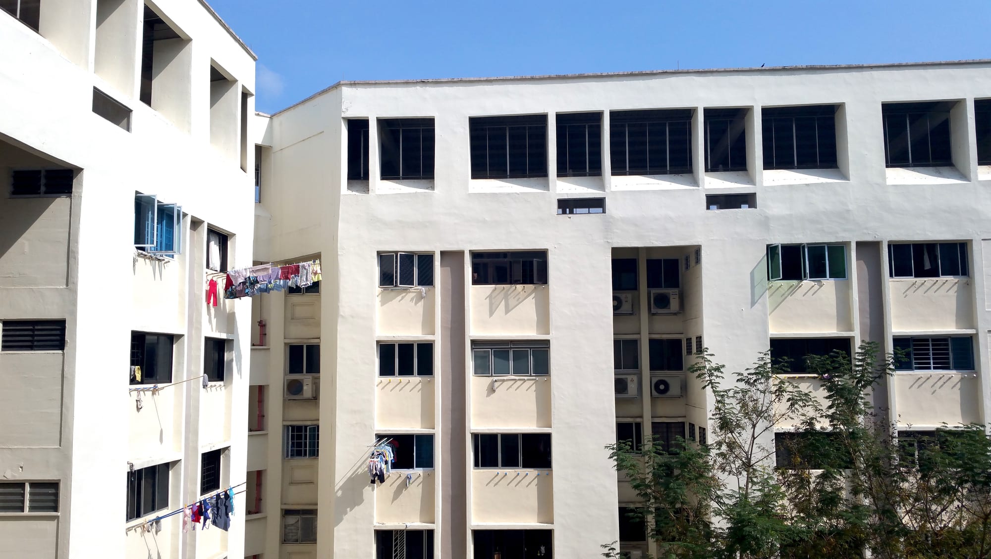 Cream-coloured HDB apartment blocks in daylight, with laundry hanging from bamboo poles outside several windows