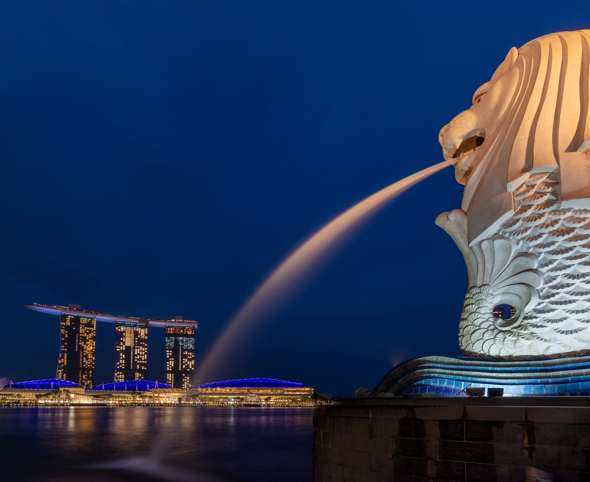 A statue with a lion's head and a fish's body spouting water into a bay