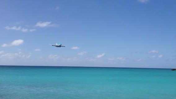 A large jet aircraft flying extremely low over a beach full of onlookers just before landing