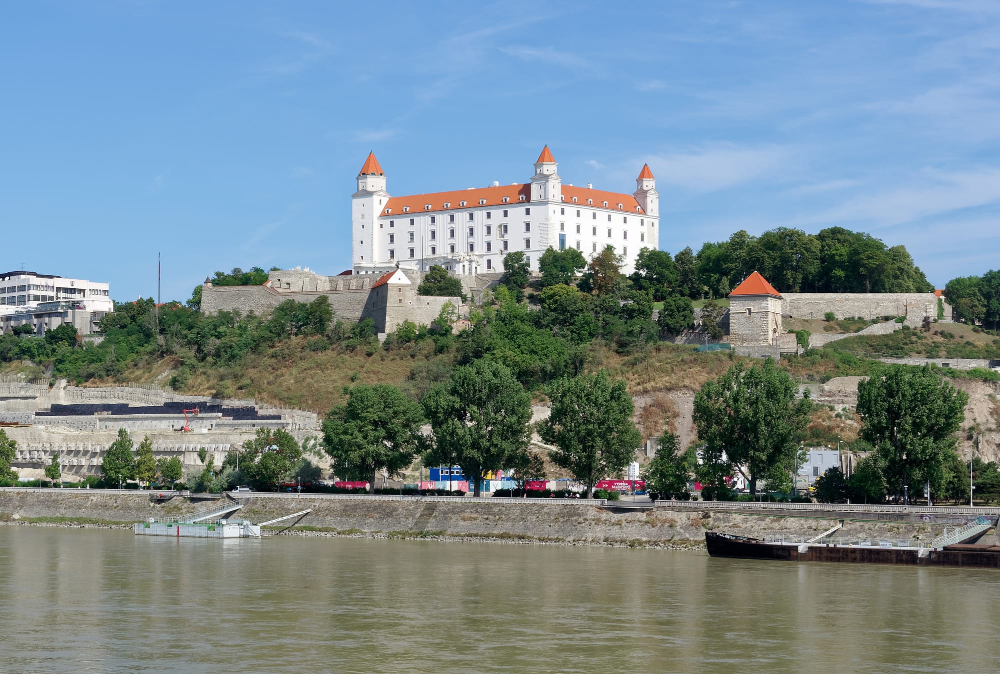 A large square white castle with four corner towers on a hill above a city