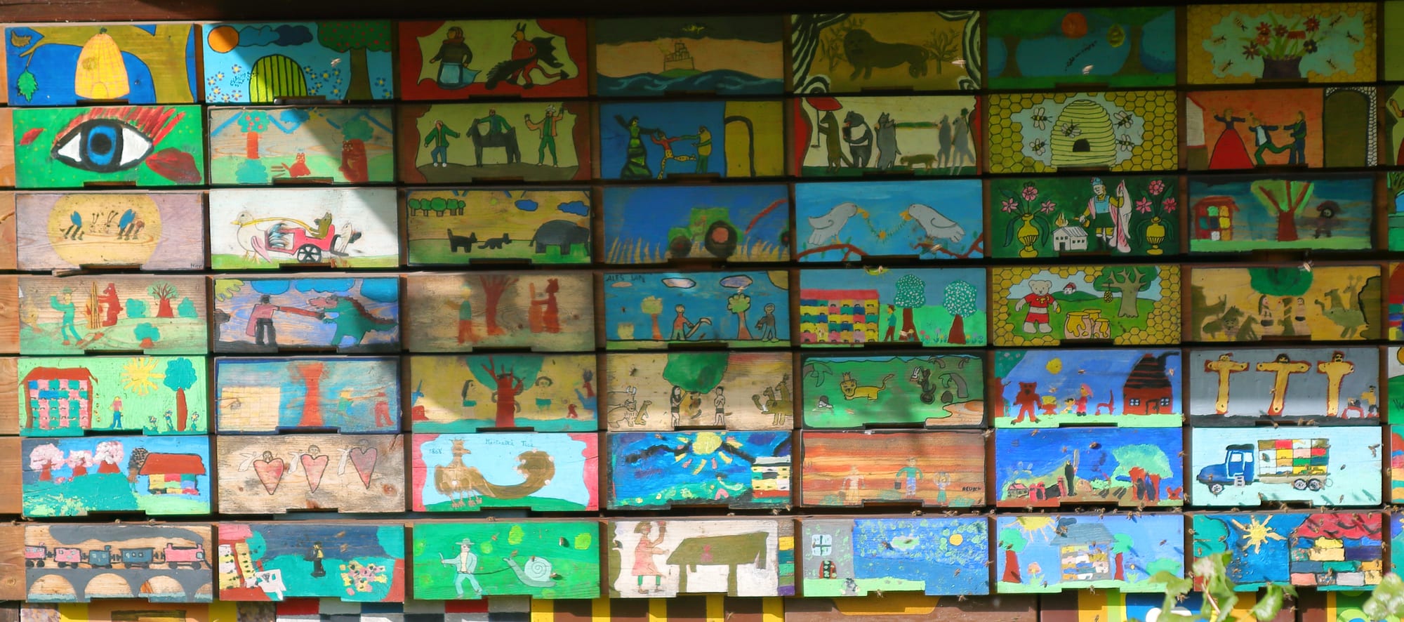 A wall of small wooden beehive drawers, each with a brightly painted folk-art scene on its front panel