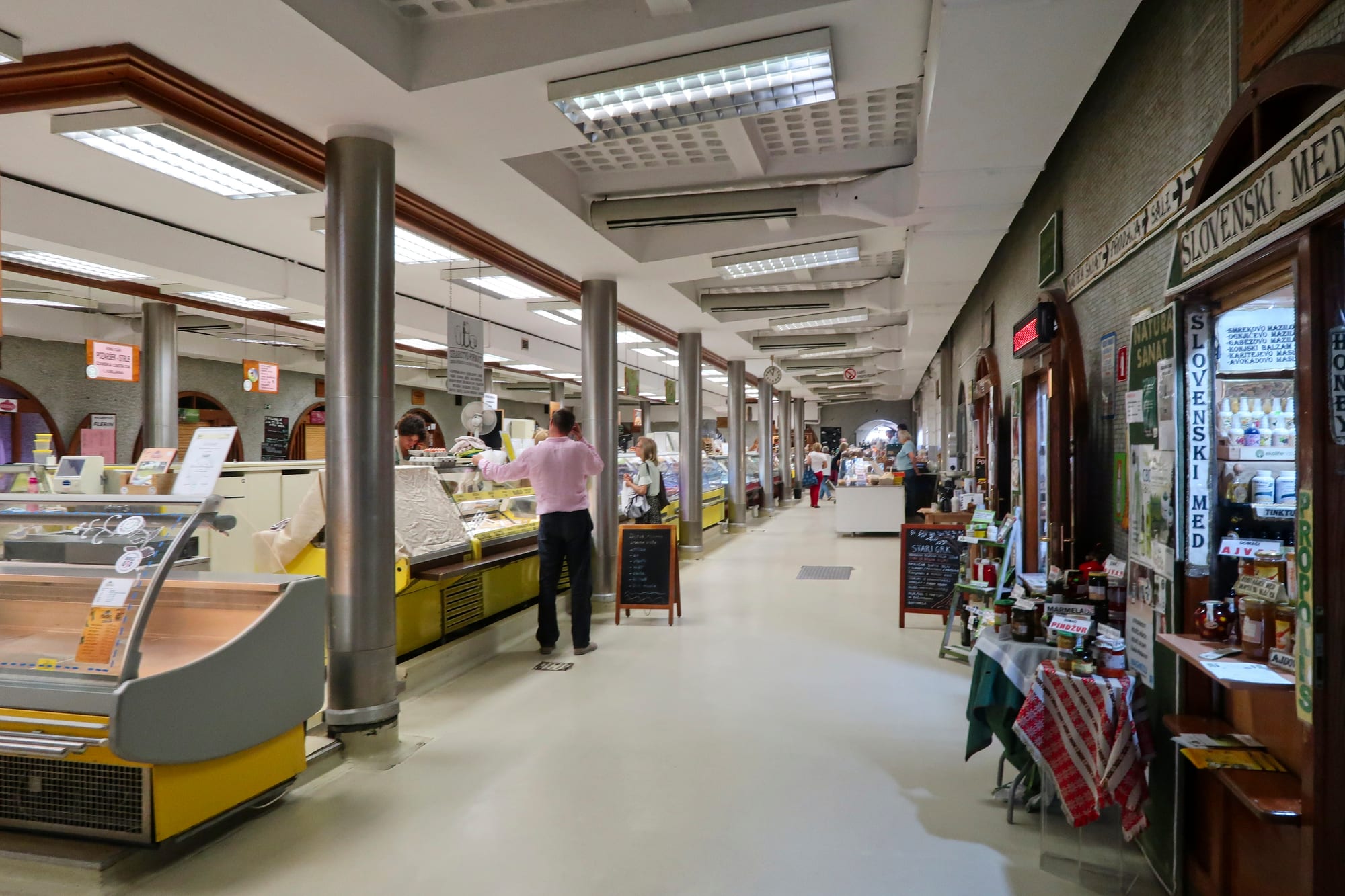 Shoppers and stallholders inside the covered arcade of Ljubljana's Central Market, with deli counters and a Slovenian honey stall