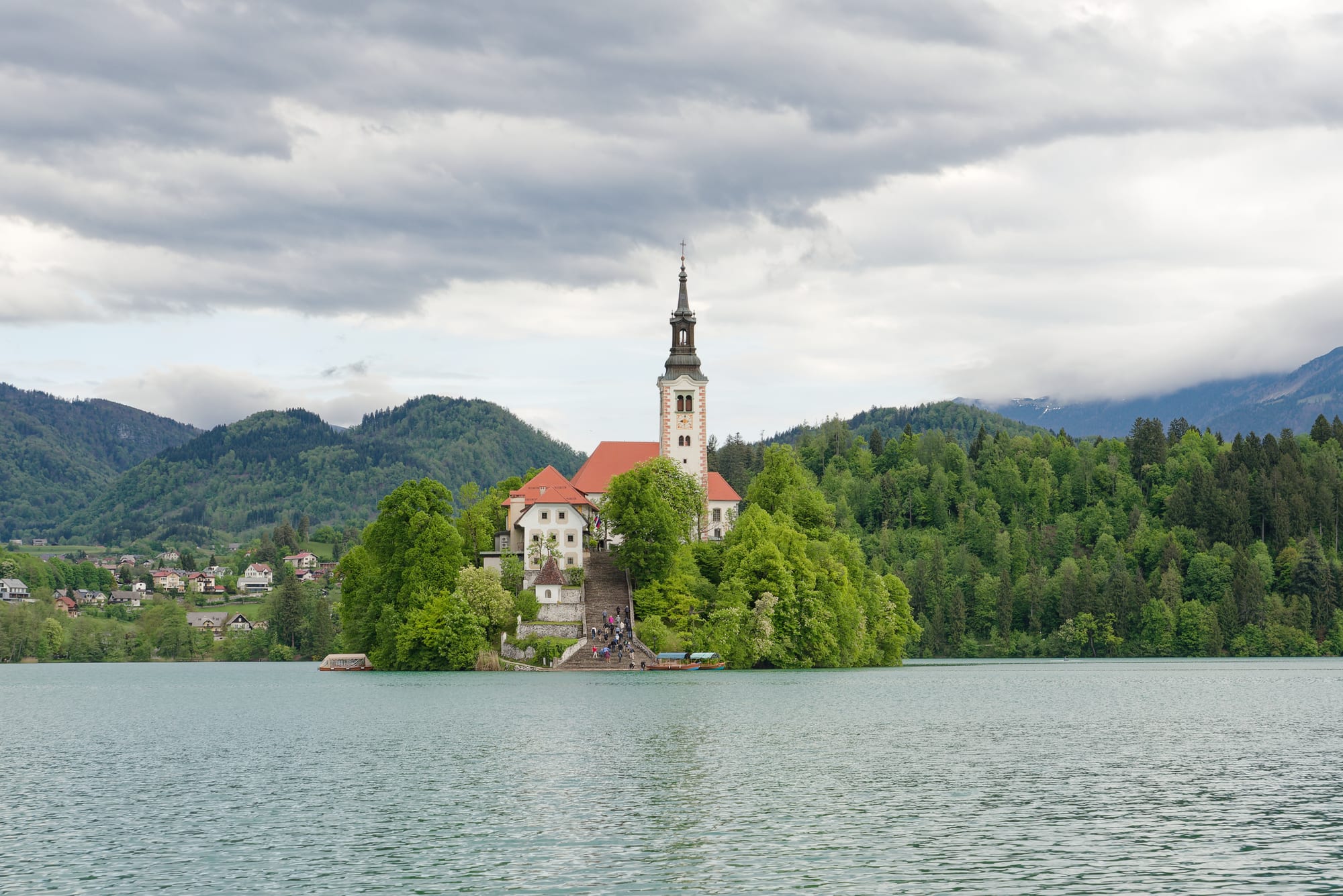 A small island with a church tower in the middle of a calm alpine lake