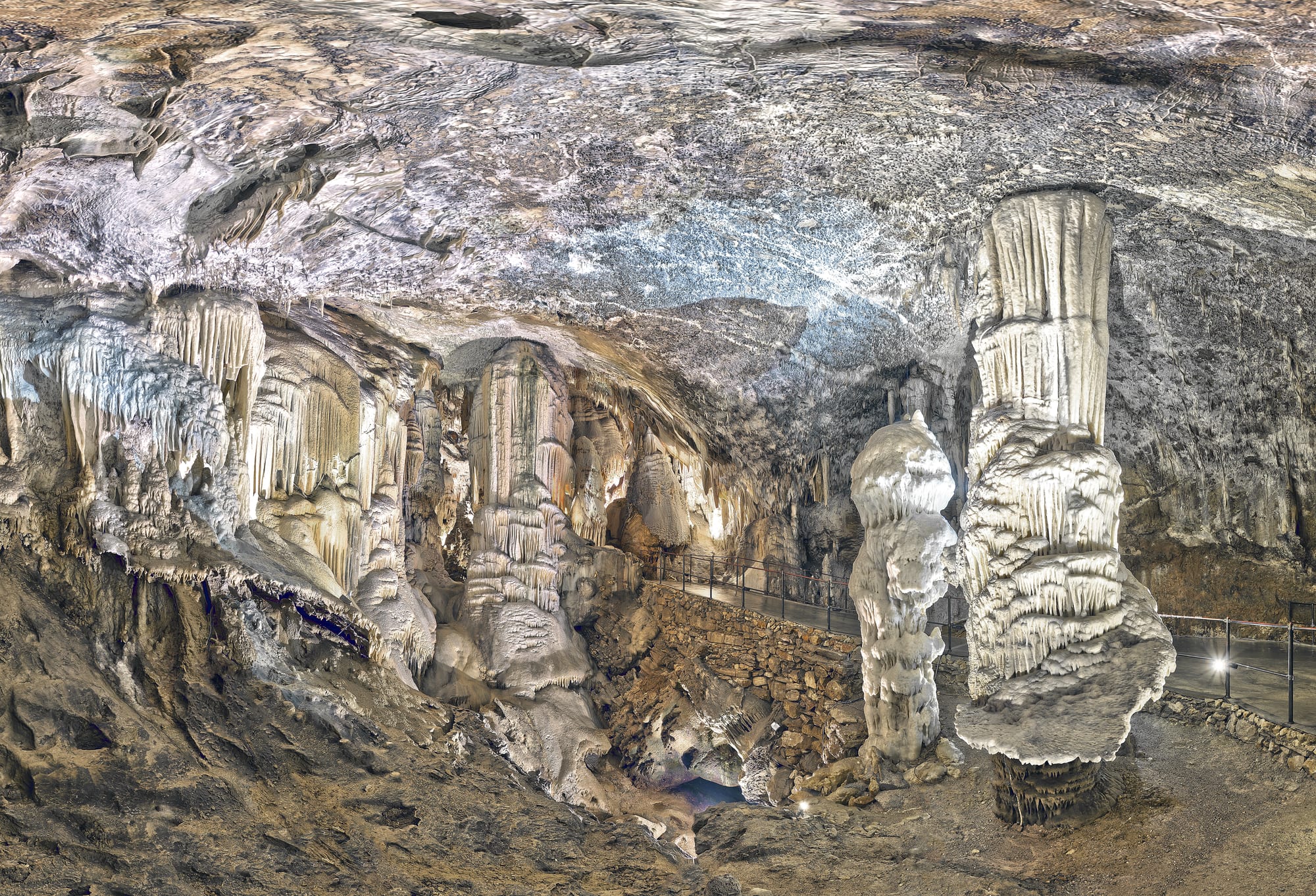 A vast illuminated limestone cave chamber with stalactite formations