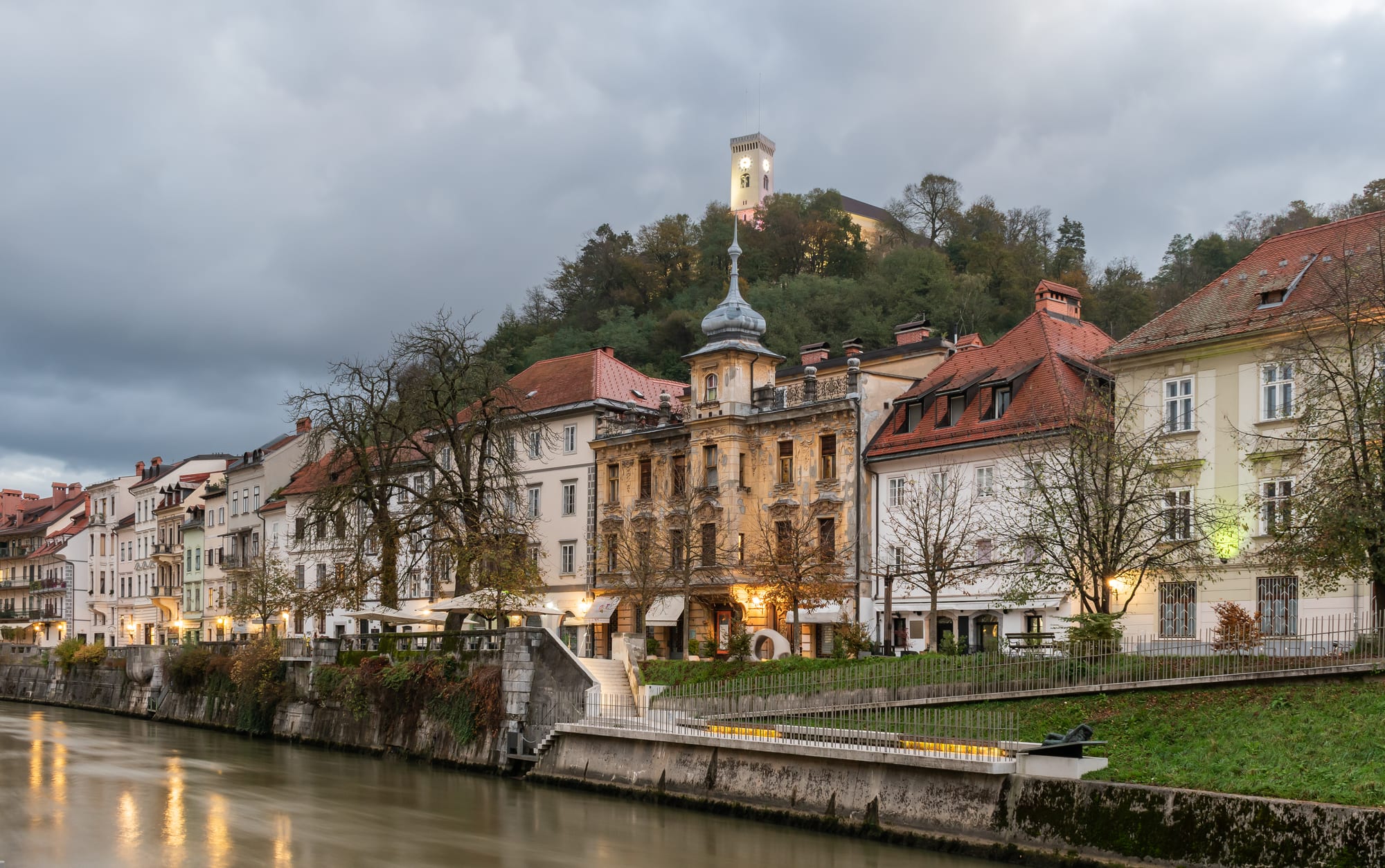 Riverside baroque and pastel buildings along the Ljubljanica river in central Ljubljana with the castle above