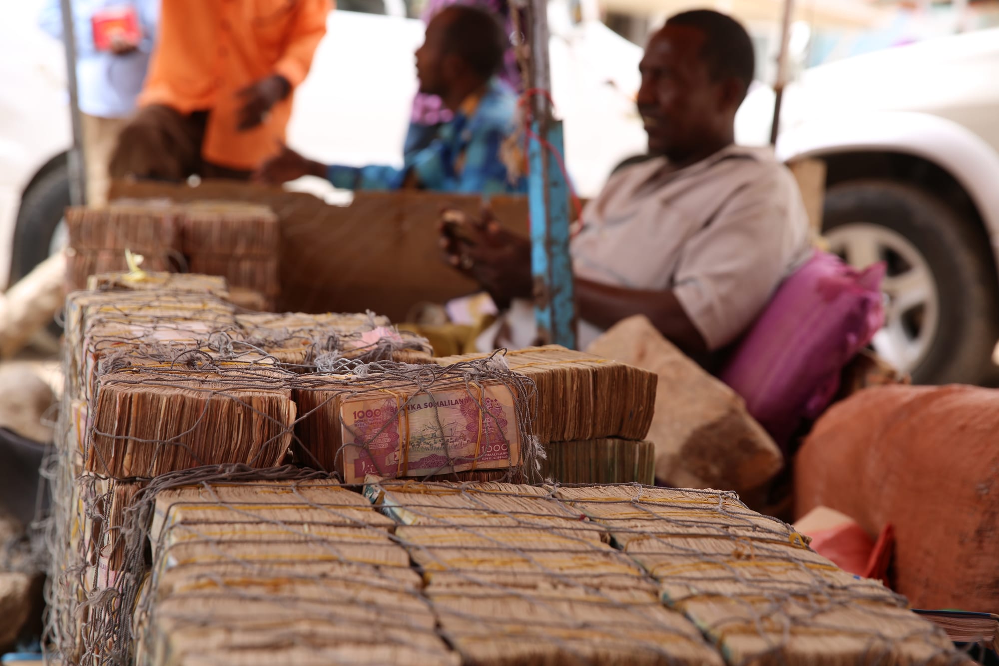 Large string-tied bundles of Somaliland shilling banknotes stacked on a street stall