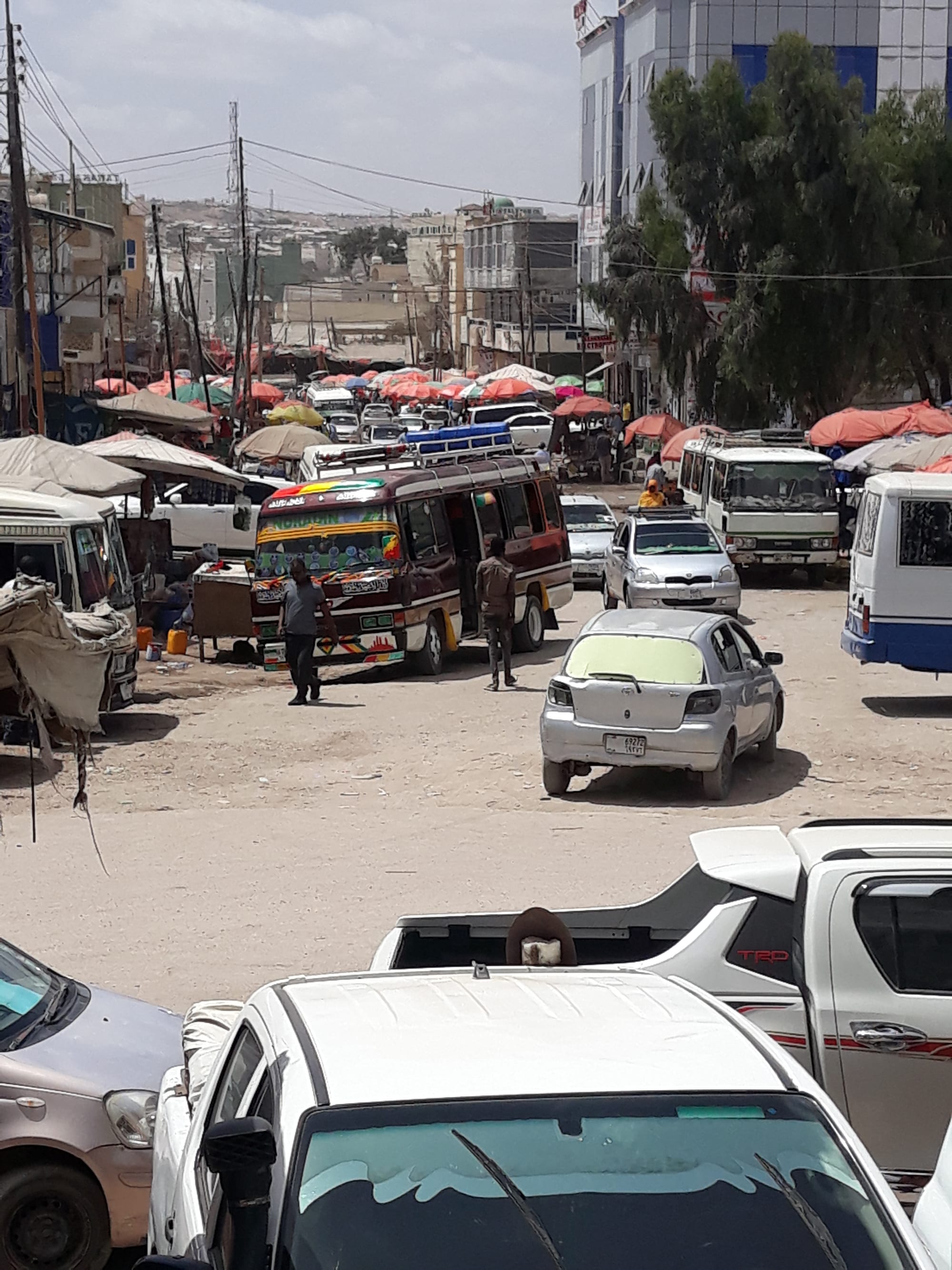 A busy Hargeisa street crowded with minibuses, cars and market stalls under awnings, with pedestrians moving between the vehicles