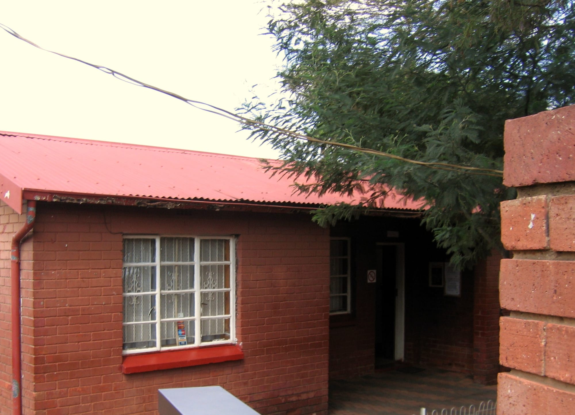 A small brick house with a red corrugated-iron roof on a residential street